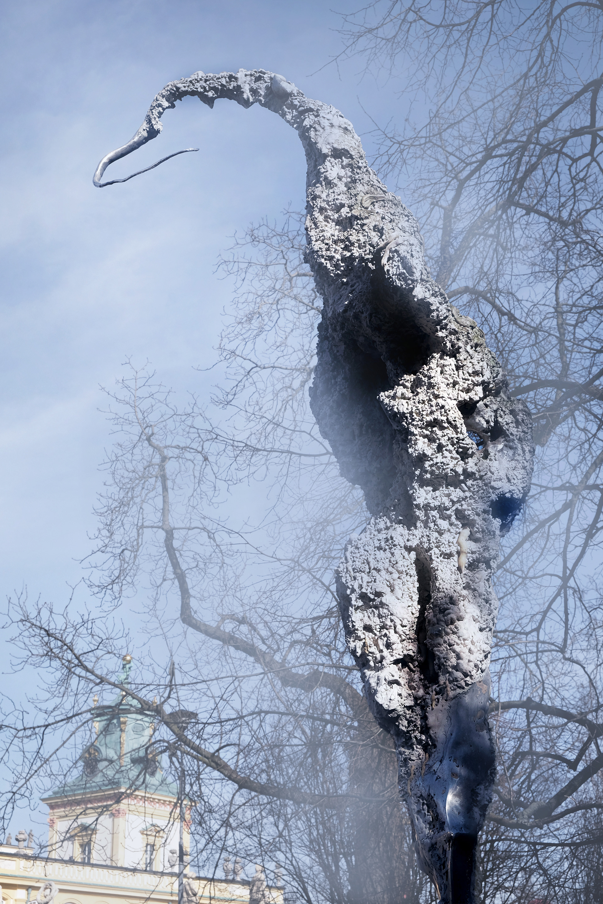 Large-scale sculpture from the Non–Humans series by Jan Gostyński, cast in bronze and aluminum with structural steel elements. The work takes the form of a hybrid, biomorphic figure with an irregular, expanding surface that evokes both organic growth and eroded matter. Shown outdoors at the Museum of King Jan III’s Palace at Wilanów, the sculpture stands in visual dialogue with the surrounding historical architecture and landscaped gardens, emphasizing the contrast between its contemporary, fragmented form and the classical setting.