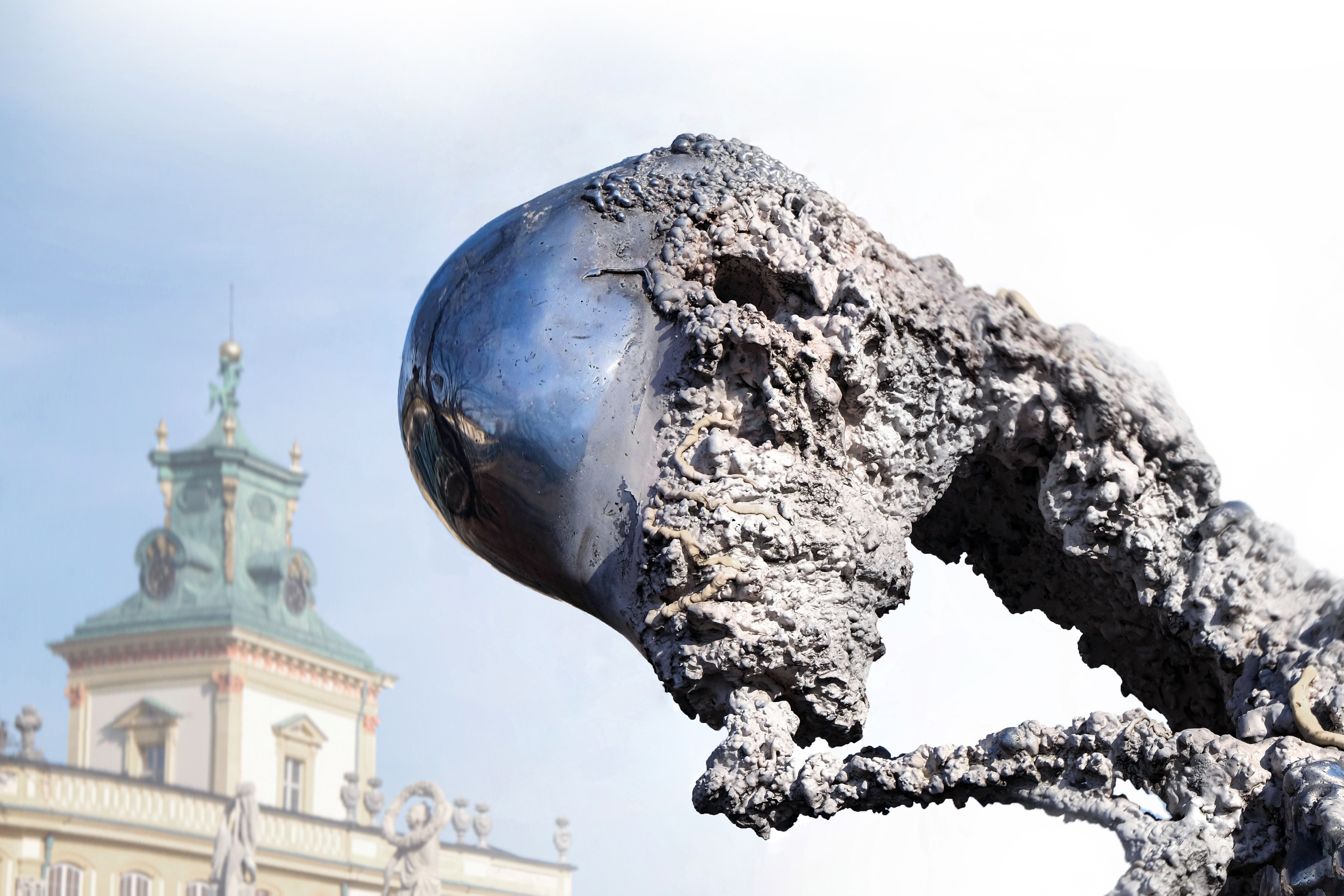 Large-scale sculpture from the Non–Humans series by Jan Gostyński, cast in bronze and aluminum with structural steel elements. The work takes the form of a hybrid, biomorphic figure with an irregular, expanding surface that evokes both organic growth and eroded matter. Shown outdoors at the Museum of King Jan III’s Palace at Wilanów, the sculpture stands in visual dialogue with the surrounding historical architecture and landscaped gardens, emphasizing the contrast between its contemporary, fragmented form and the classical setting.