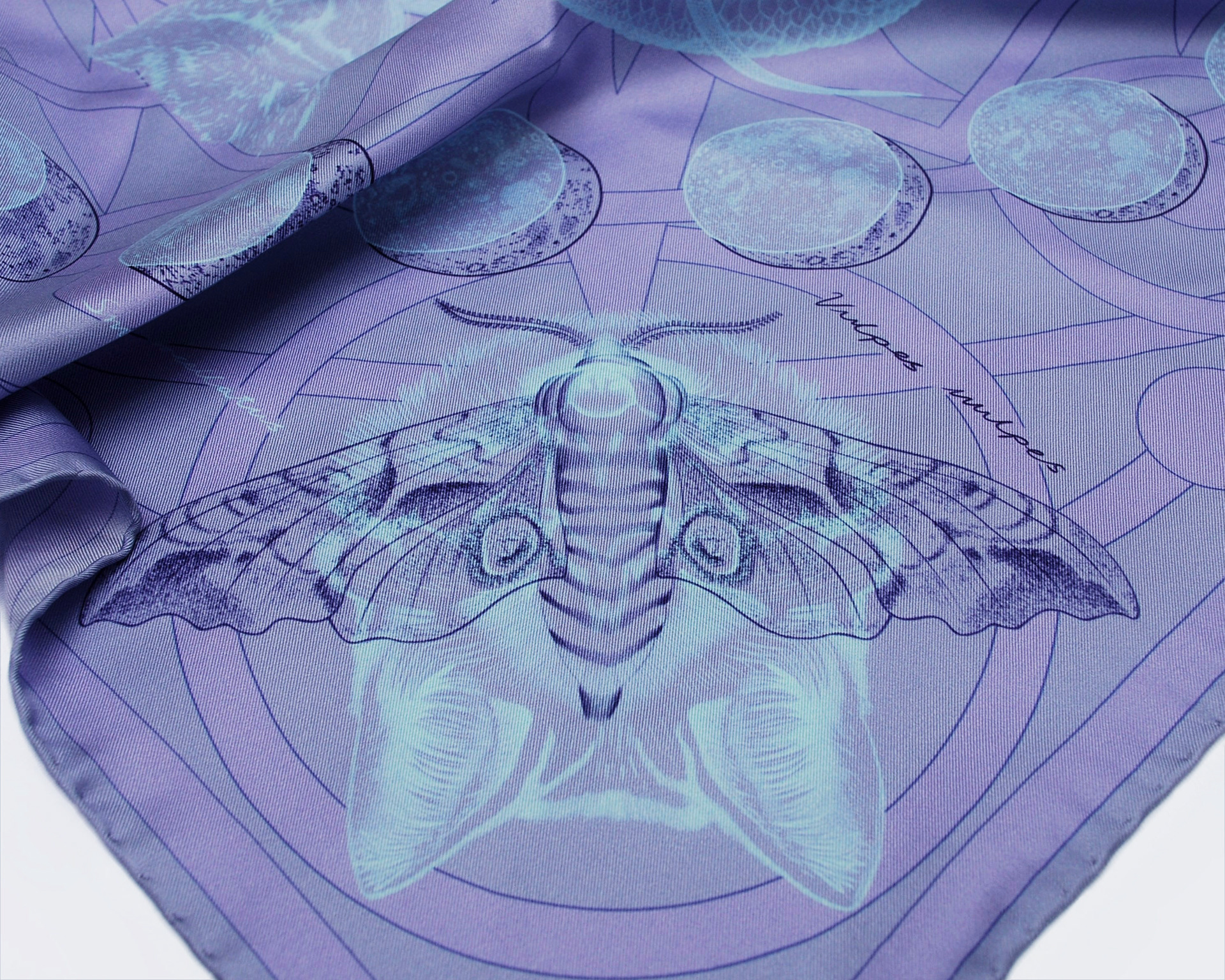 The corner of a blue silk scarf showing a moth overlaying the eyes of a fox.