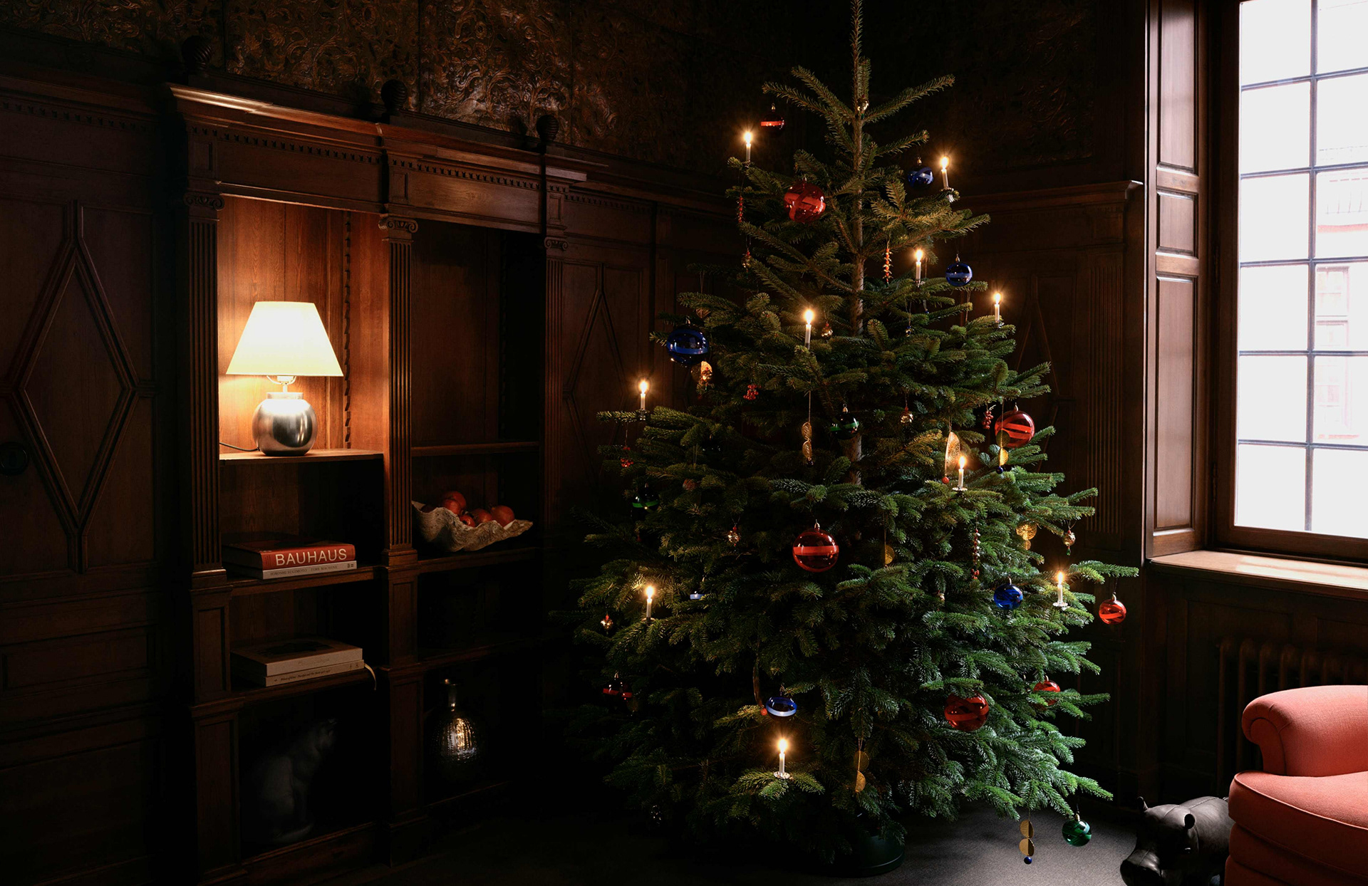 A classic wooden interior at Svenskt Tenn with a candle-lit Christmas tree adorned with brass and glass ornaments from Sam Wilde’s Poison of Eden collection.