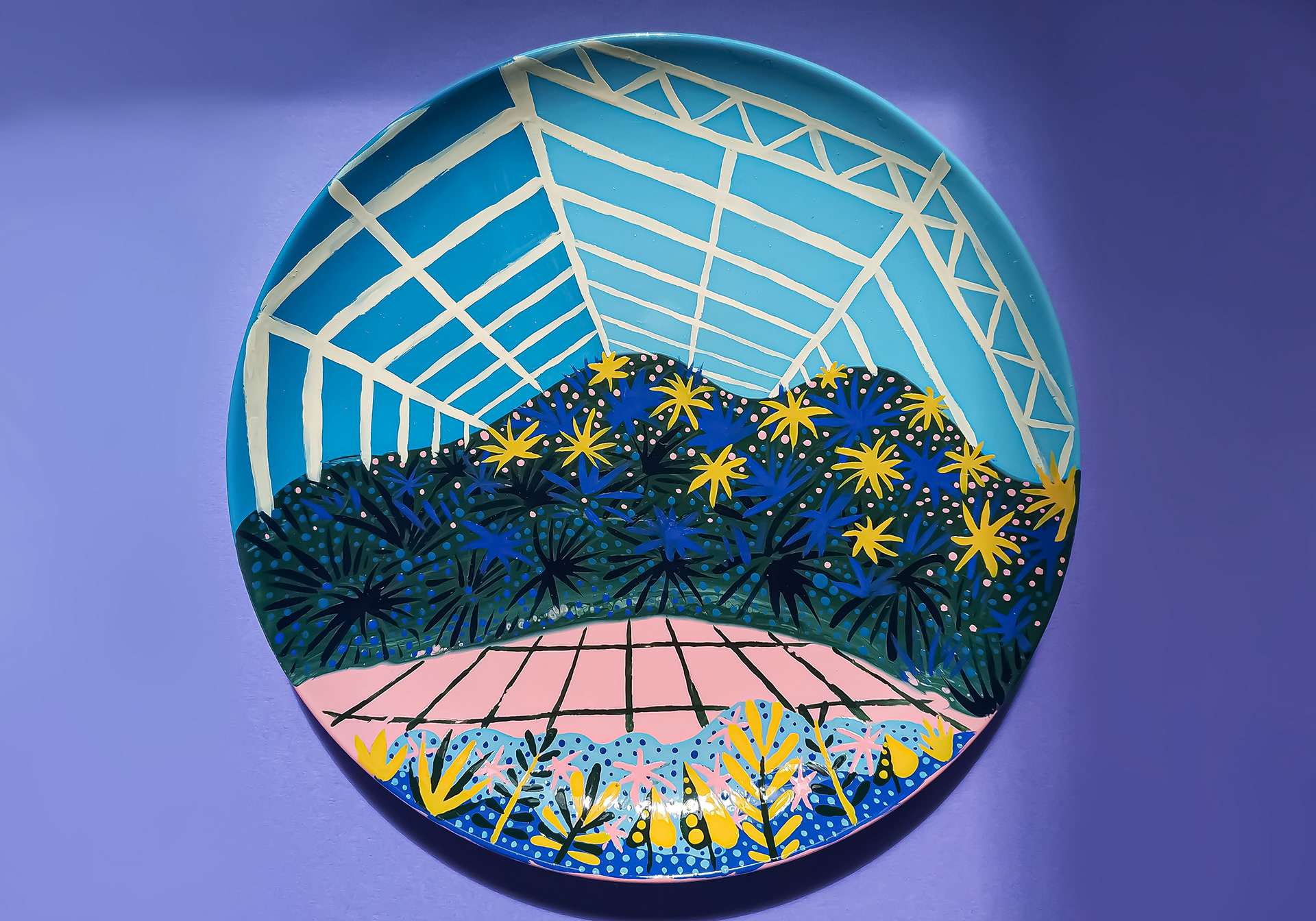 Blue hand-painted ceramic plate of an abstract greenhouse scene with tiled pink flooring.