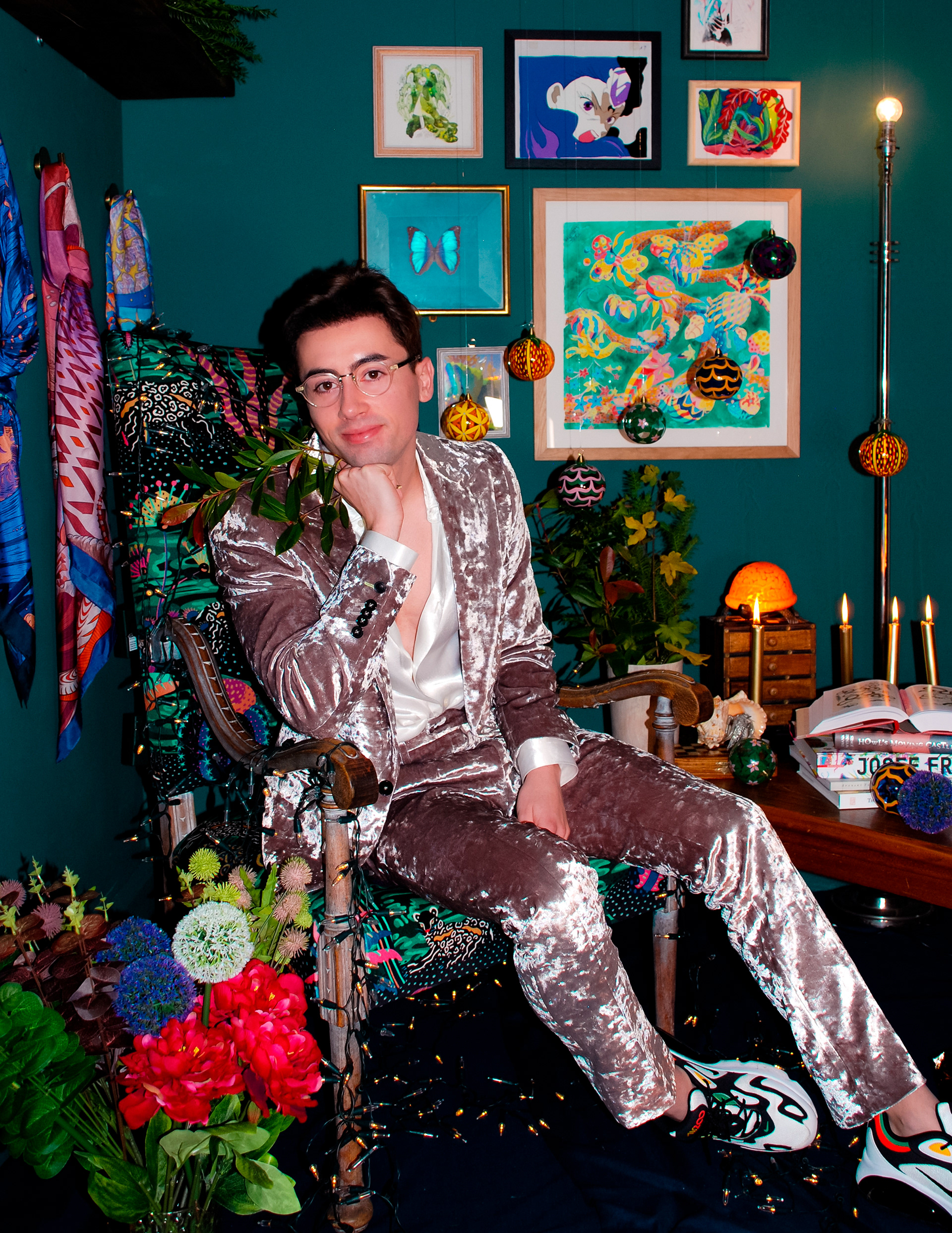 Sam Wilde wearing a crushed velvet silver suit sitting in a patterned arm chair.