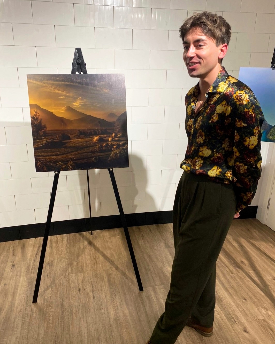 Sam Wilde smiling while standing next to a canvas created using AI software.