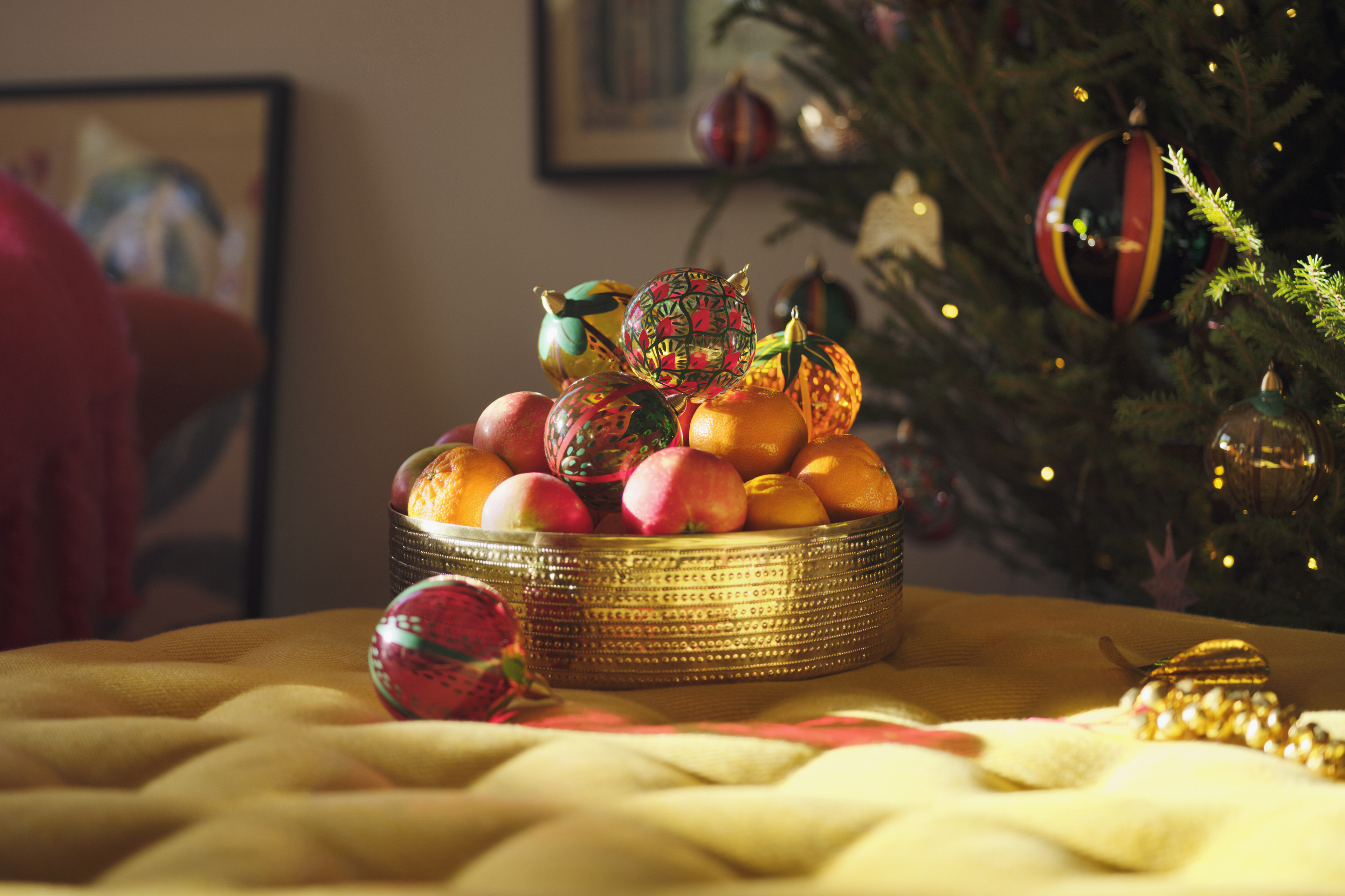 A bowl of oranges in the sun light mixed with glass Christmas baubles by Sam Wilde.