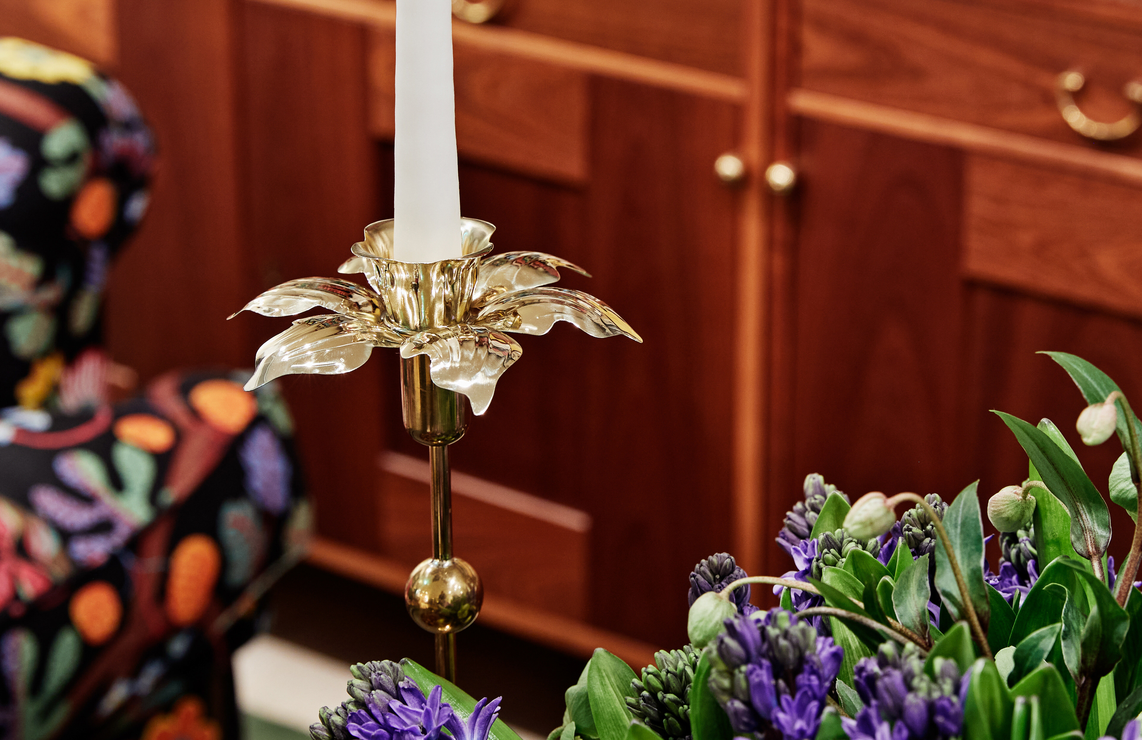 Daffodil brass candle ring designed by Sam Wilde next to a bouquet of flowers at Svenskt Tenn.