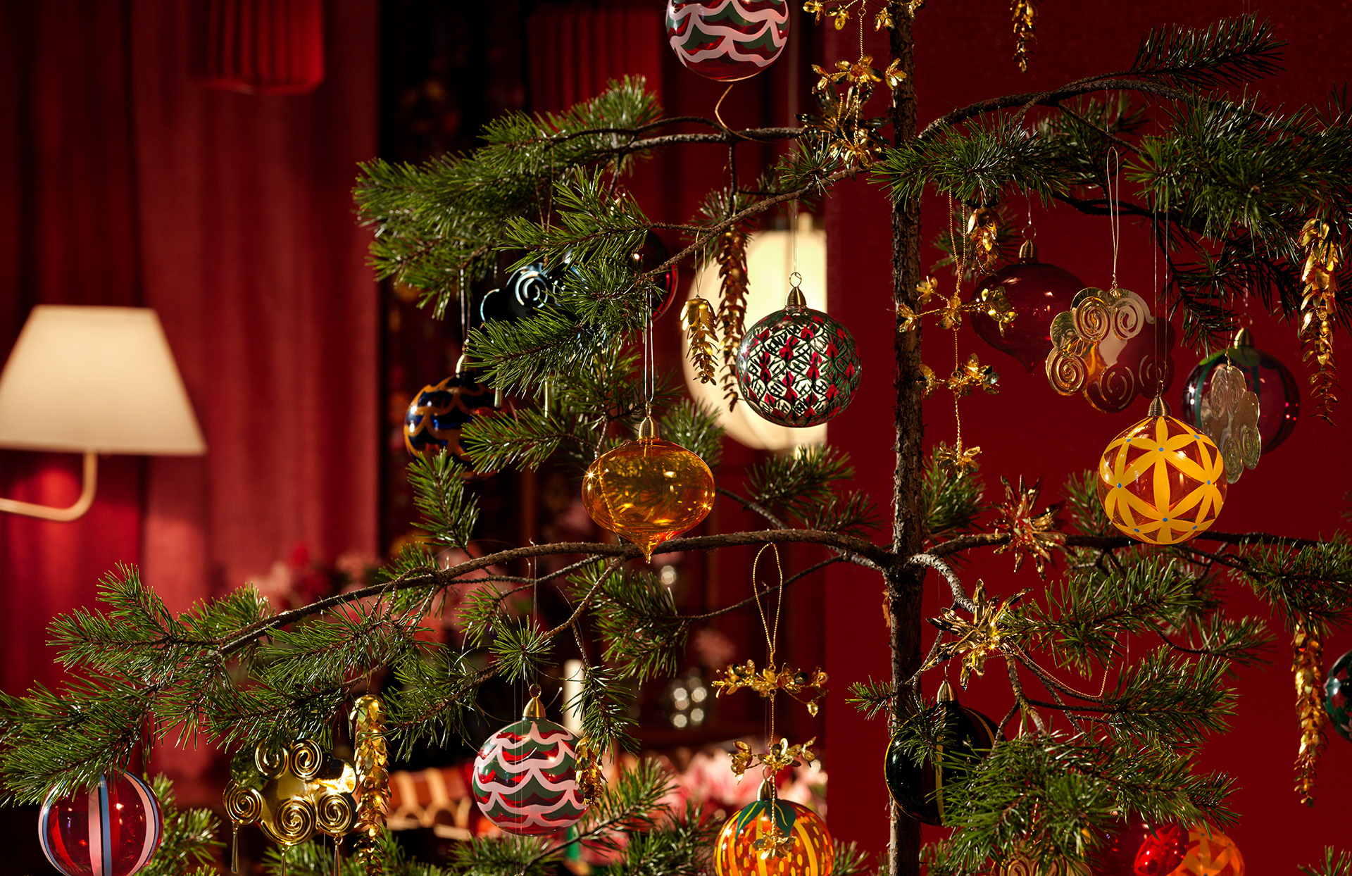 Christmas tree in a warm red living room featuring glass baubles designed by Sam Wilde for Svenskt Tenn.