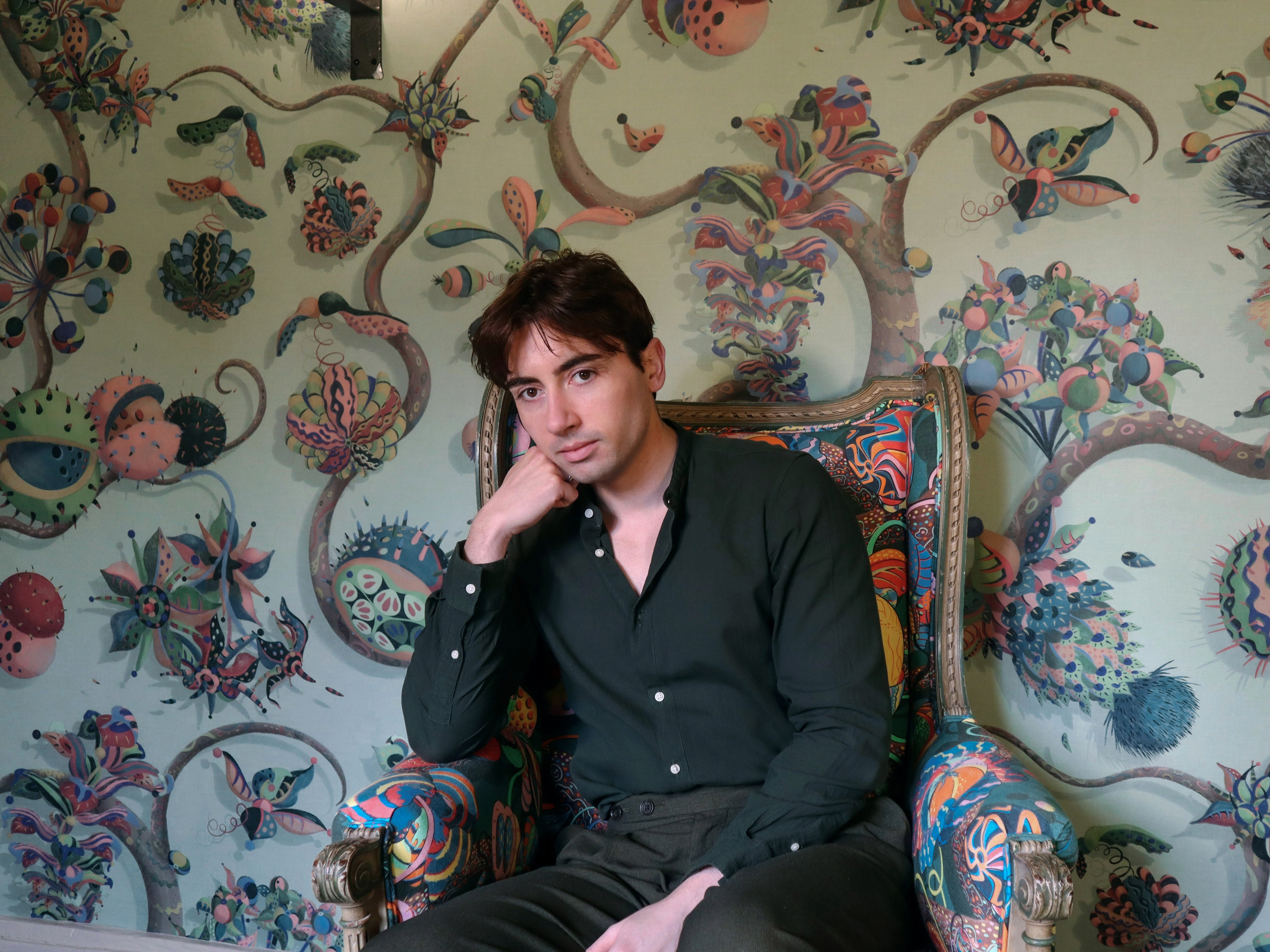 Wallpaper and pattern artist sits in front of sage green hand-painted tree wall art mural.