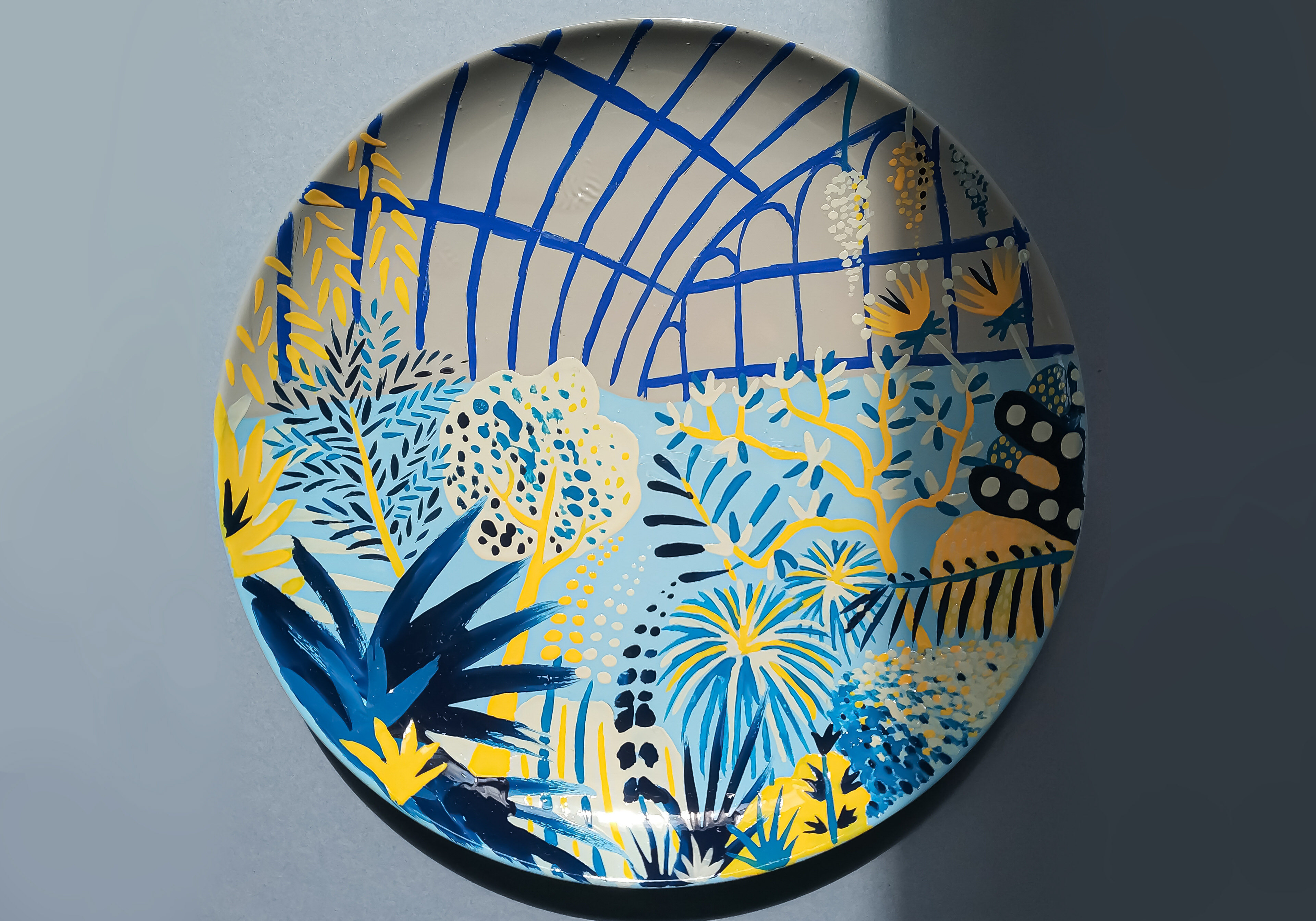 Hand-painted ceramic showing the inside of a greenhouse in grey, blue and yellow colours.