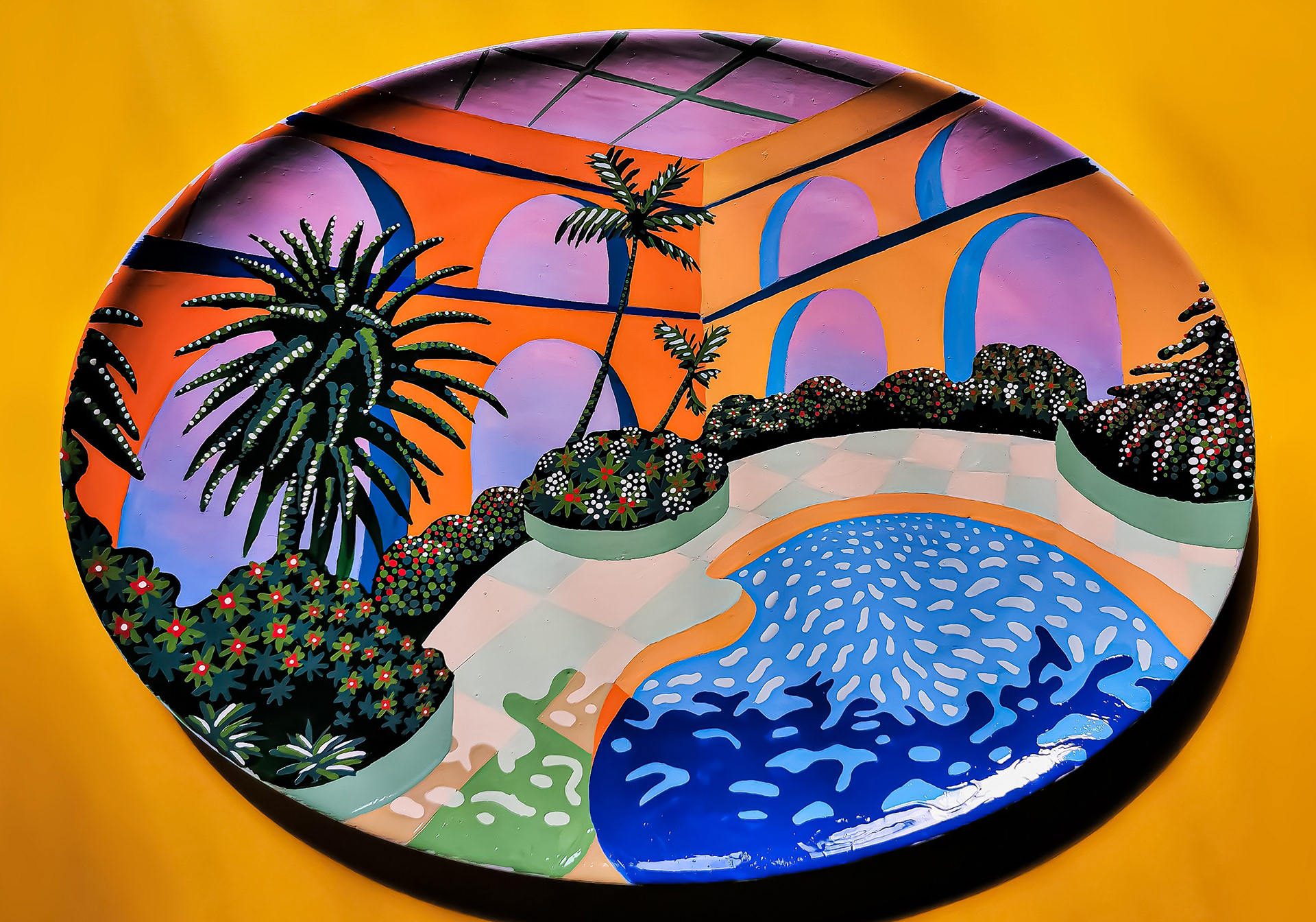 Hand-painted oval ceramic depicting a pool, orange archways and palm trees in vibrant colours.