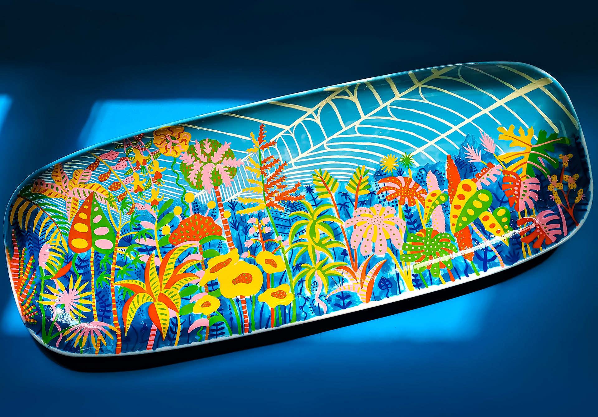 A hand-painted oblong ceramic dish depicting a vibrant greenhouse scene bursting with plants.
