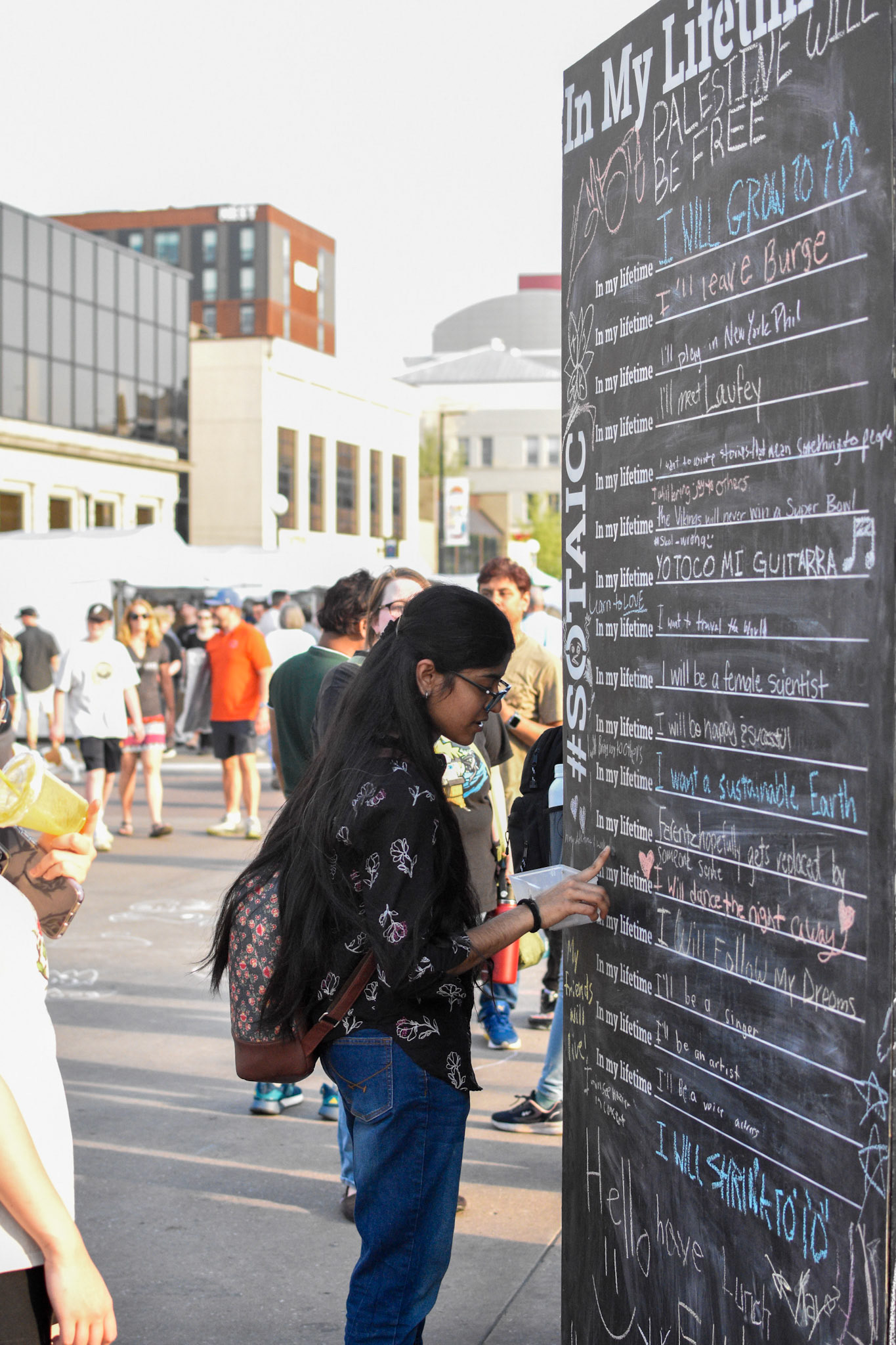 IOWA CITY, IOWA/UNITED STATES – JUNE 6, 2025: A woman adds her message to the “In My Lifetime” chalkboard at the Iowa Arts Festival in downtown Iowa City.
