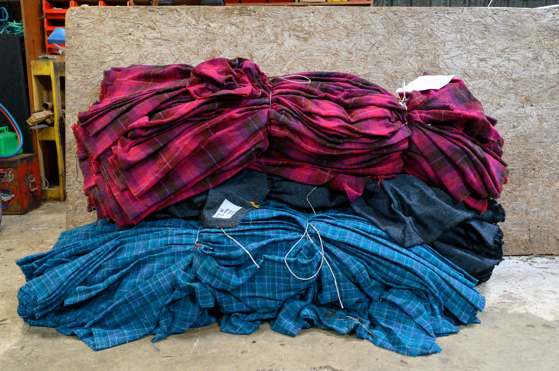 Completed cloths.
Anna Morrison works as a darner for the Shawbost mills. She checks the lengths of Harris tweed for mistakes and loose threads. A lose thread sounds easier, as it must be only tied off and into the cloth.
This 70m length of Harris tweed is missing yellow thread from its pattern. Anna must weave the missing thread along the whole 70m with a needle. It is long painstaking work that needs a good eye and a patient mind.