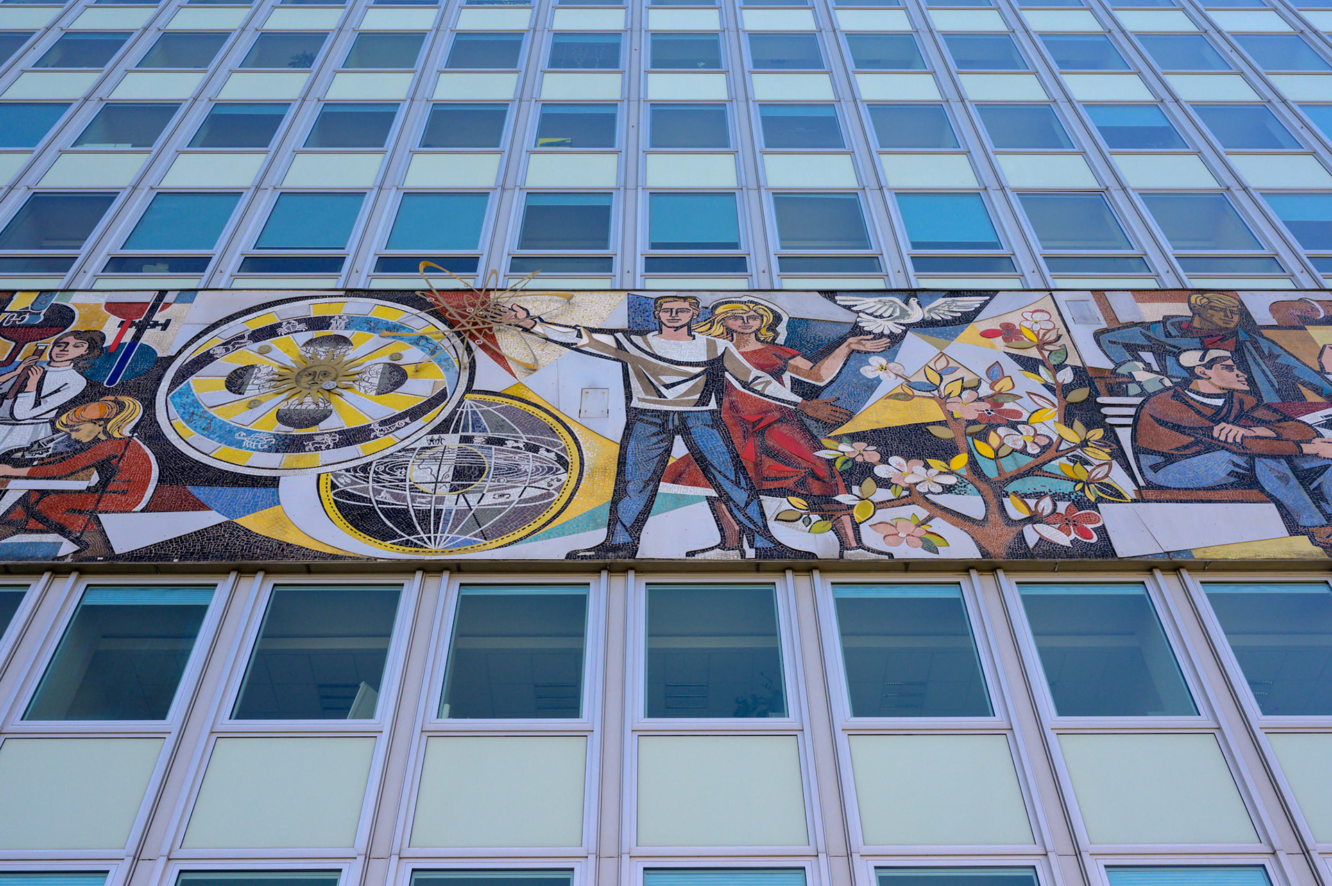 A remaining East German frieze that describes the joy of soviet progress and everyone's place in it.
Look closely and note that the man holds the atom and the woman the dove of peace. In other sections of the frieze, the woman is shown nurturing her children while the men work heroically.