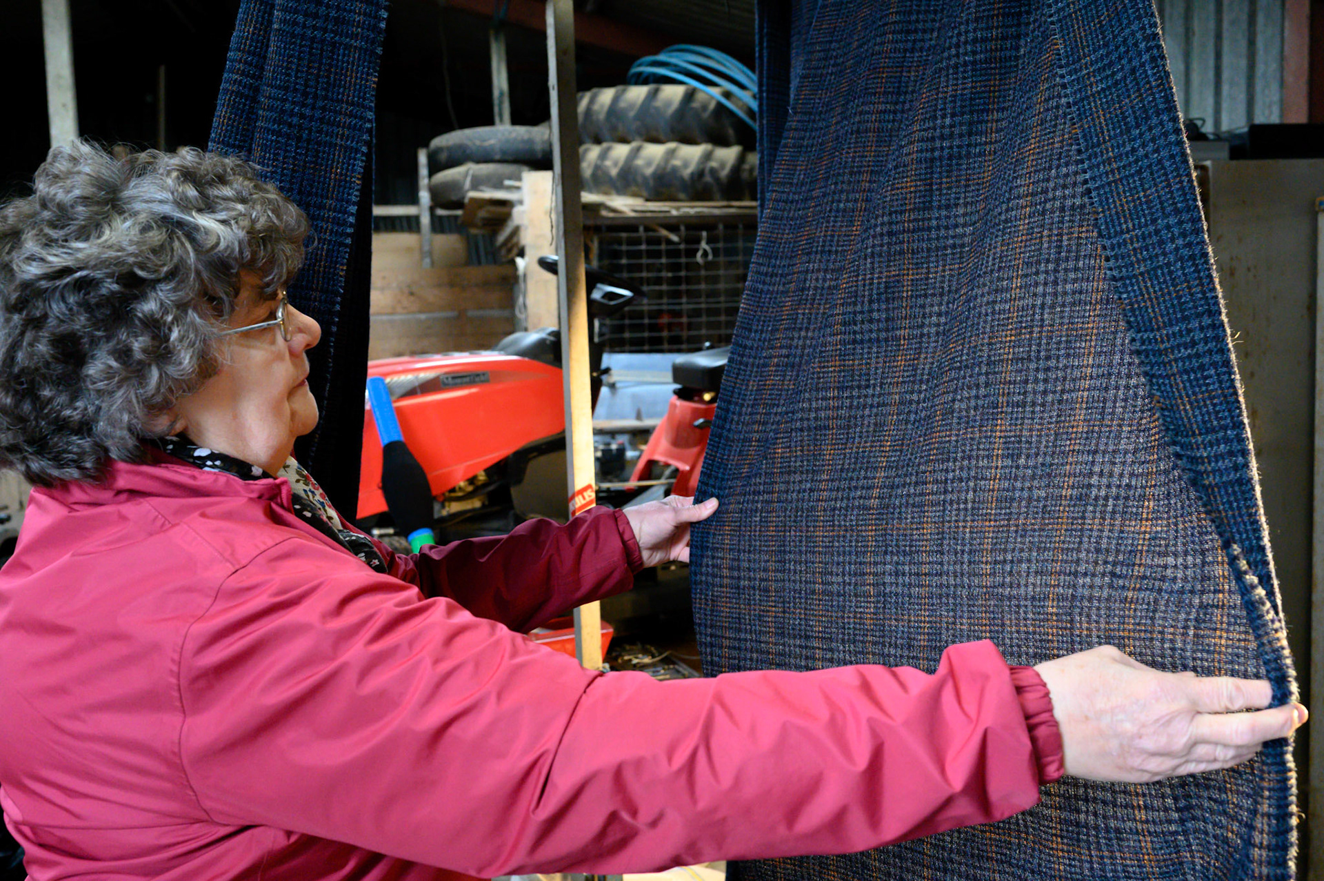 Anna Morrison works as a darner for the Shawbost mills. She checks the lengths of Harris tweed for mistakes and loose threads. A lose thread sounds easier, as it must be only tied off and into the cloth.
This 70m length of Harris tweed is missing yellow thread from its pattern. Anna must weave the missing thread along the whole 70m with a needle. It is long painstaking work that needs a good eye and a patient mind.