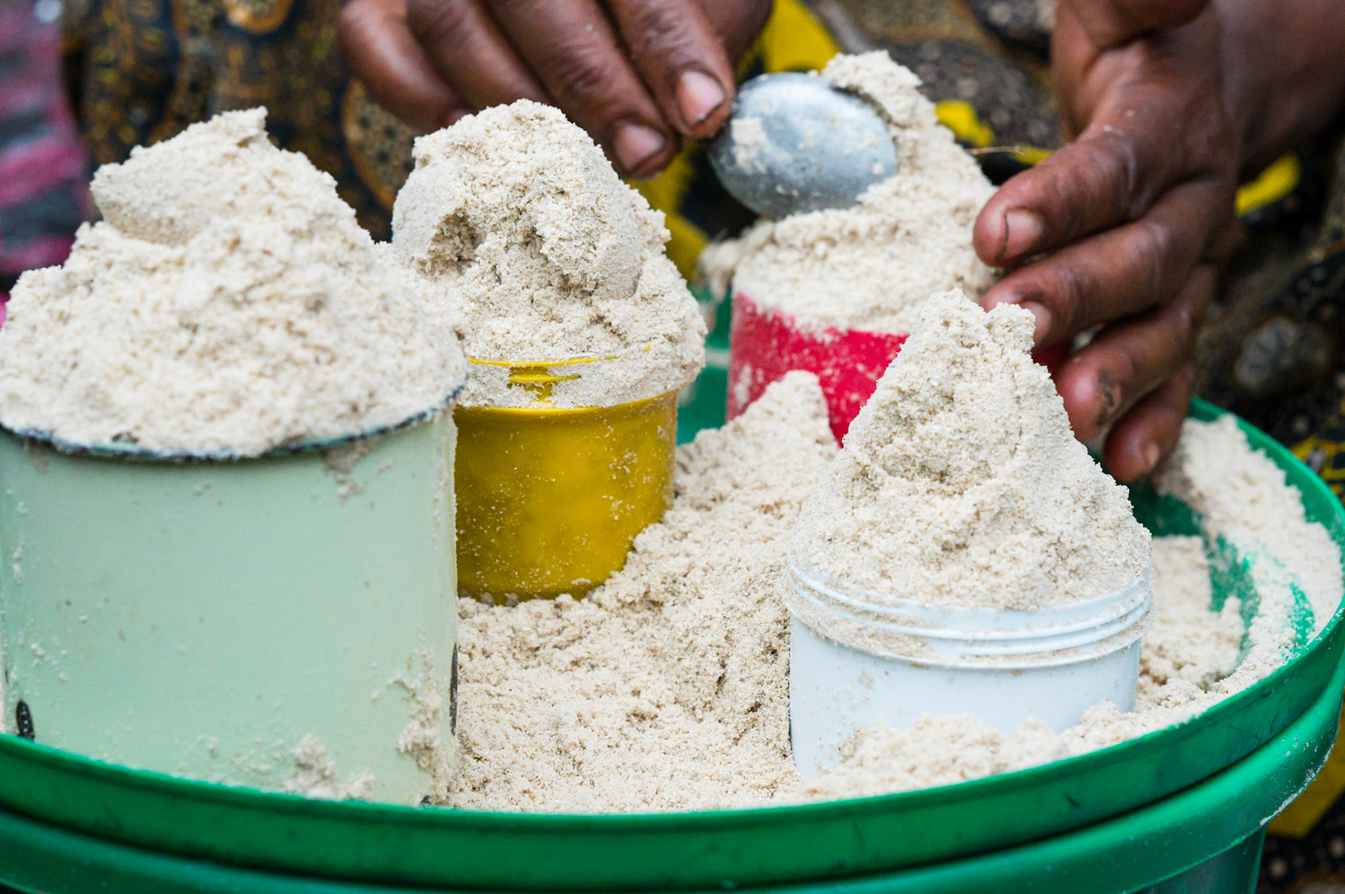 A woman measuring flour into a dried leaf, folded and tied a package.