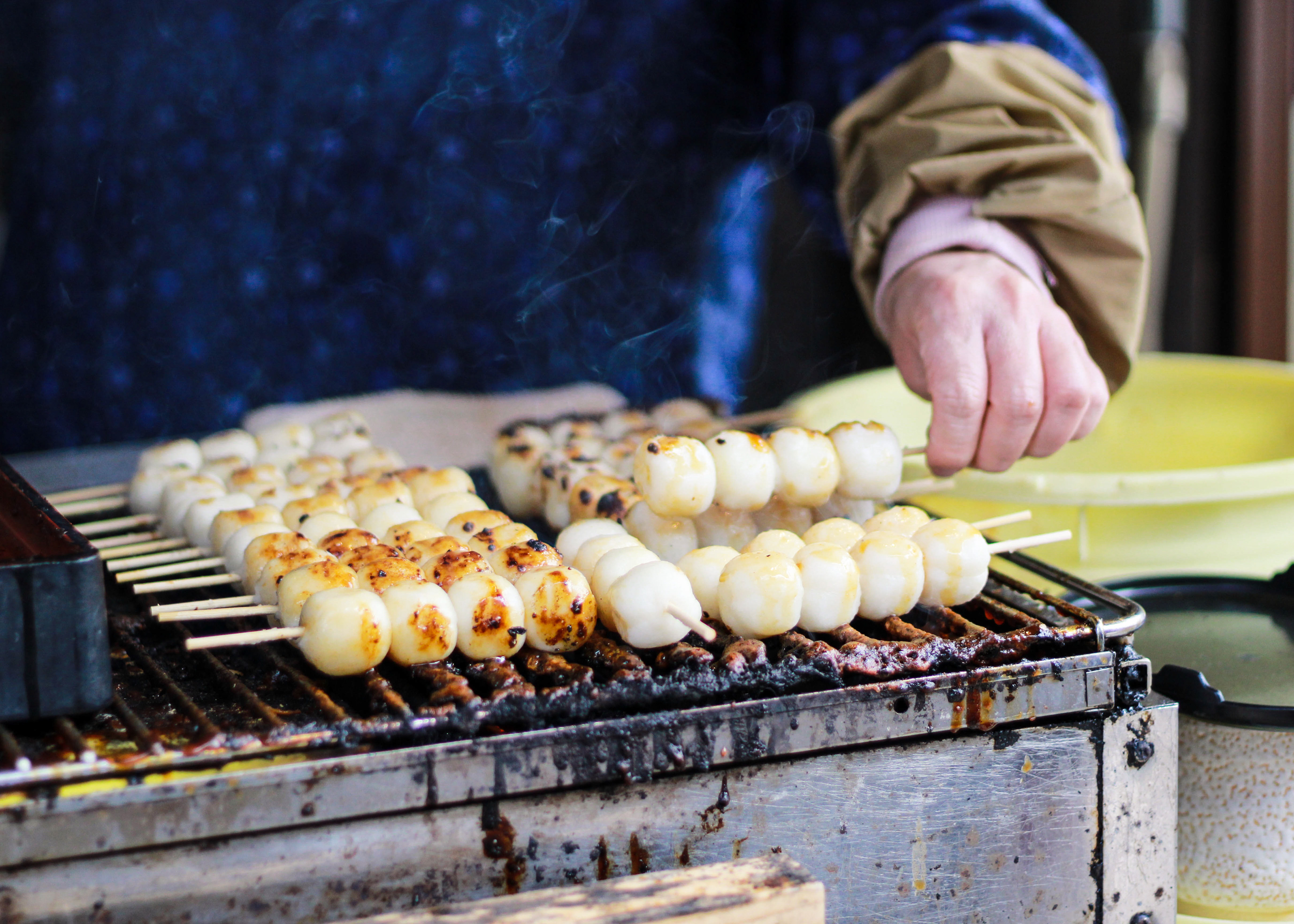 A street vendor heats dango as it cooks.