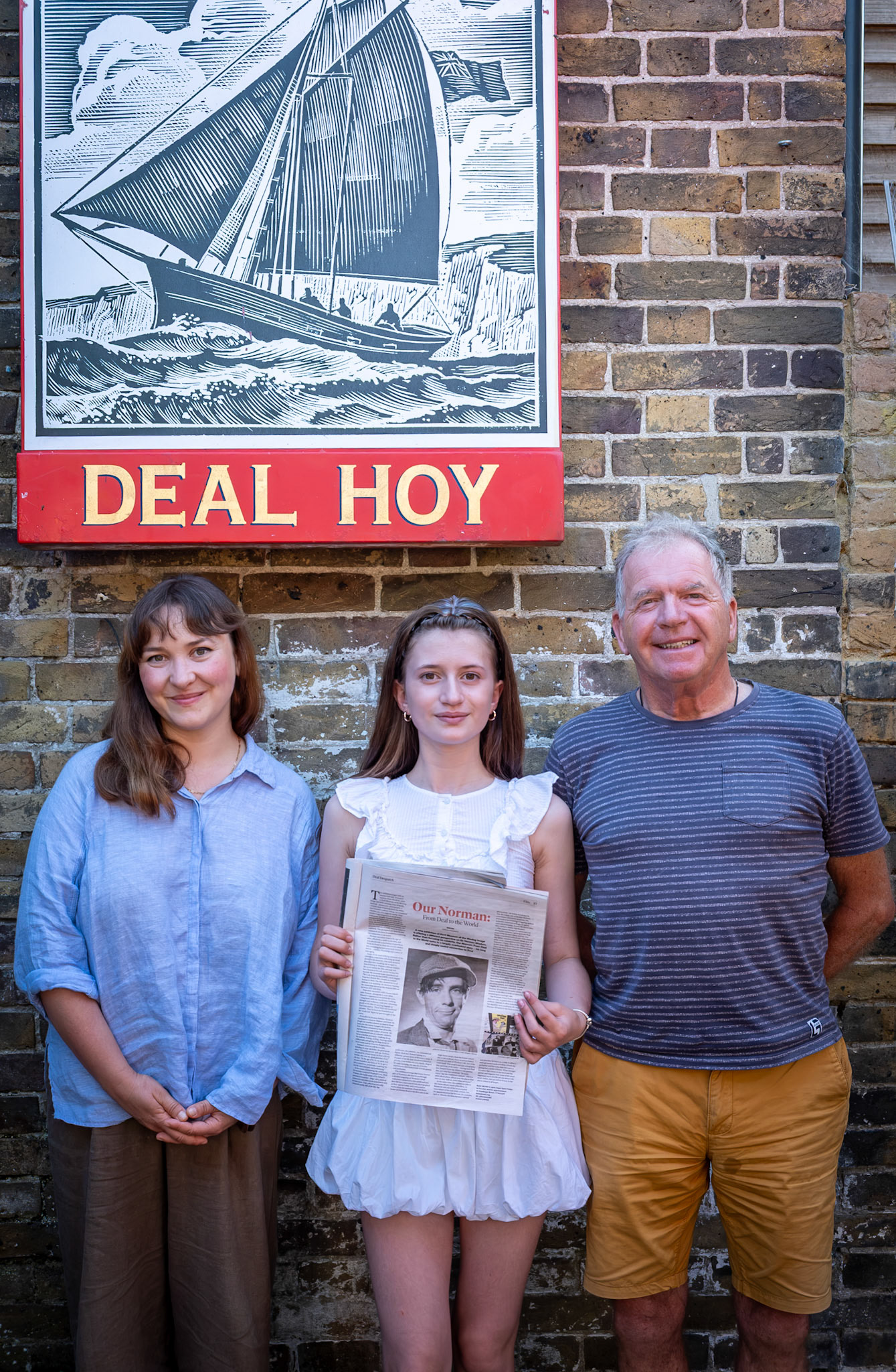 Norman Wisdom lived in Deal from the age of nine and continued to return even after he became famous. A new exhibition at Kent Museum of the Moving Image in Deal focuses on his deep connection with Deal: "Our Norman: From Deal to the World".  Natasha Poljakowa (left in the picture) wrote the article for the Deal Despatch and remembers that even in the Soviet Union where she grew up, people flocked to the village cinema near the polar circle to watch his films. Children "ran away from school to watch them". Norman's relatives still live locally. 12 year old Ruby, in the centre, is his great neice and the gentleman on the right is his nephew. Launch of The Deal Despatch, Deal Hoy, 2nd July, 2026.
