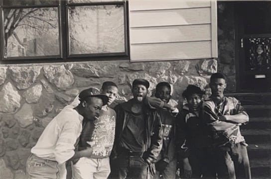 Black and white photograph of a group of six young boys posing together in front of a house.