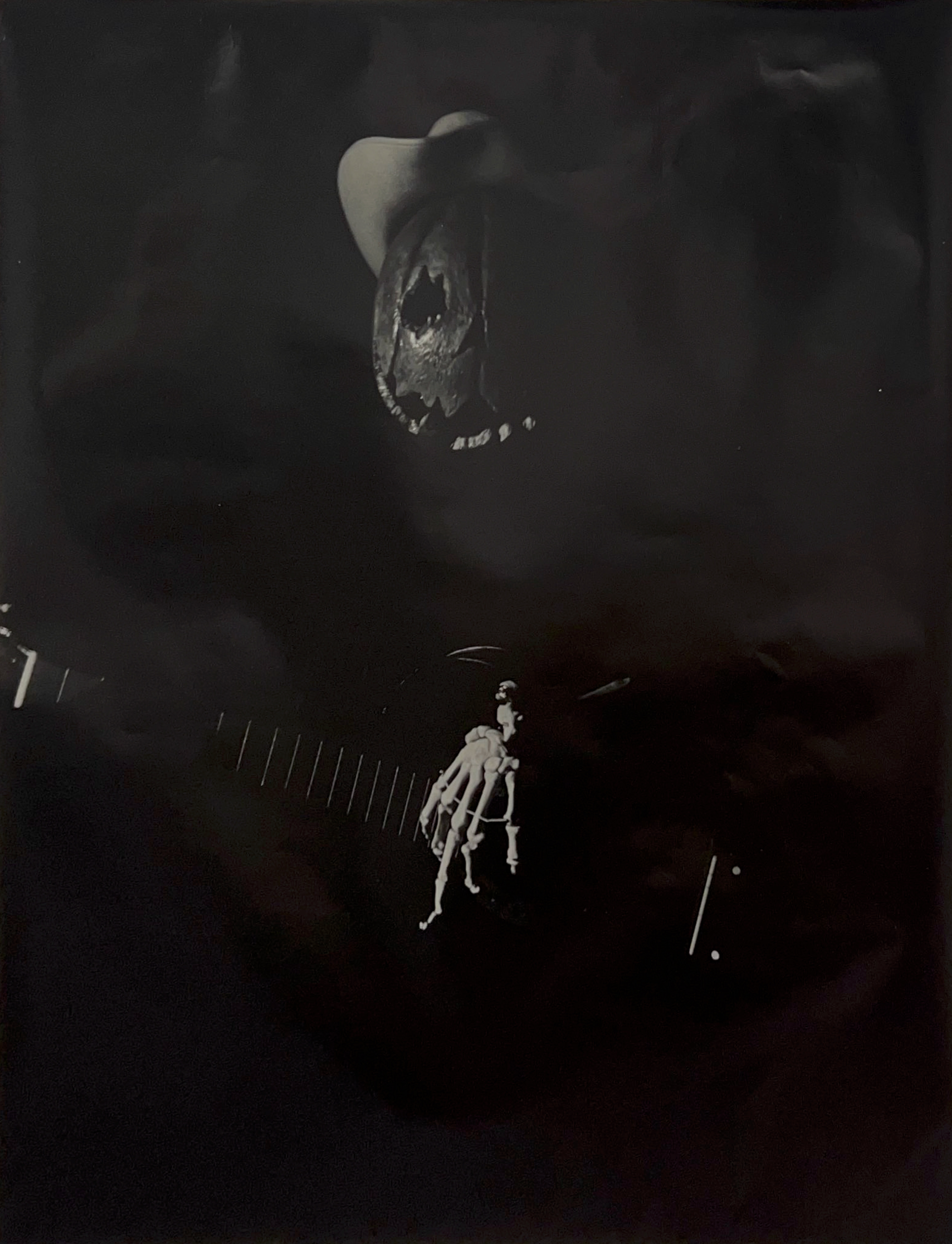 Black and white photograph of a pumpkin-head figure wearing a cowboy hat and strumming a guitar with a skeleton hand.