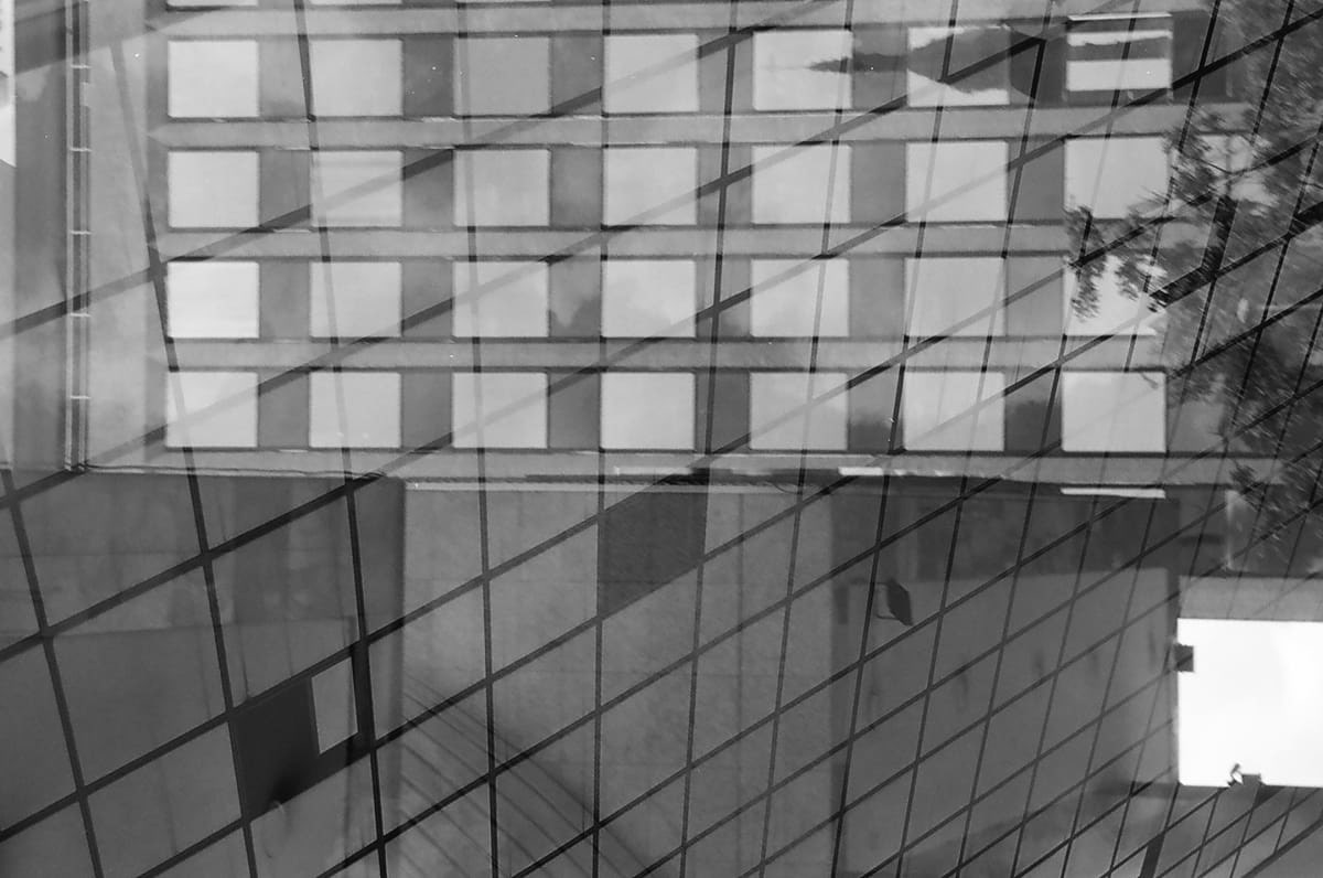 Black and white photo of a building reflected in another glass building