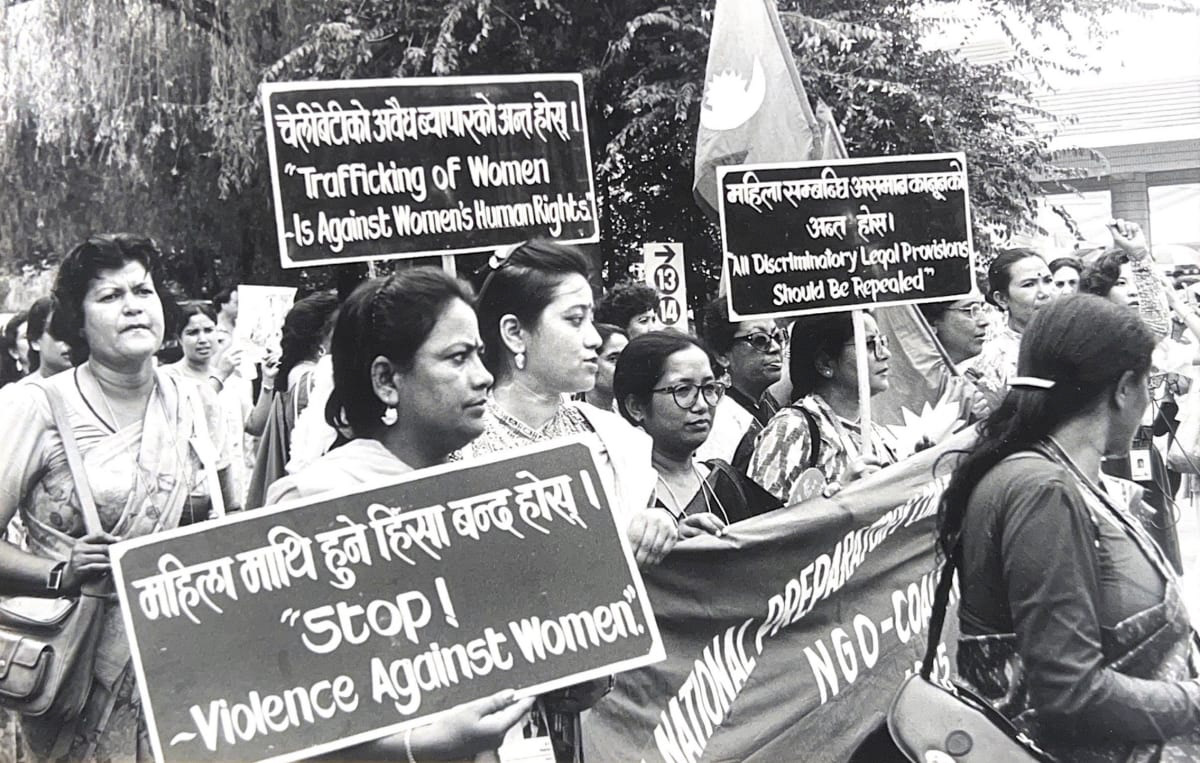 A black and white photograph of women marching in a protest and holding signs. The signs are written in two languages and say "stop violence against women," "trafficking of women is against human rights," and "all discriminatory legal provisions should be repealed."