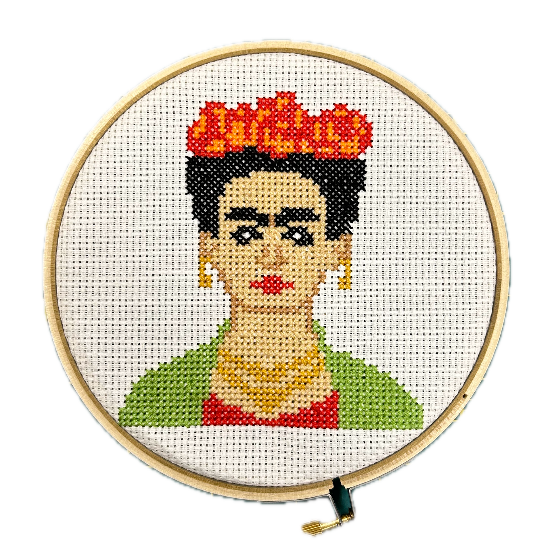 Cross-stitch portrait of Frida Kahlo on an embroidery ring. Frida has red flowers in her hair, a red and green top, and gold earrings and the necklace.