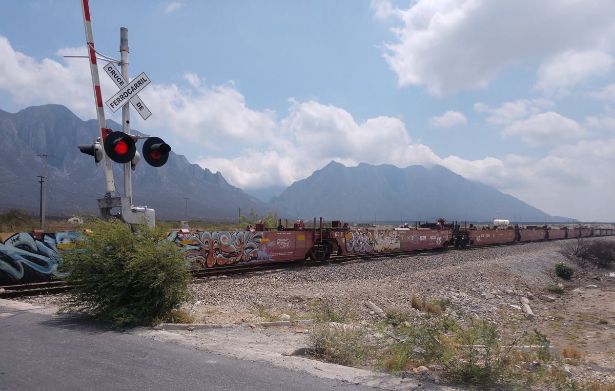 color photograph of a graffitied freight train and crossing light with mountains in the background
