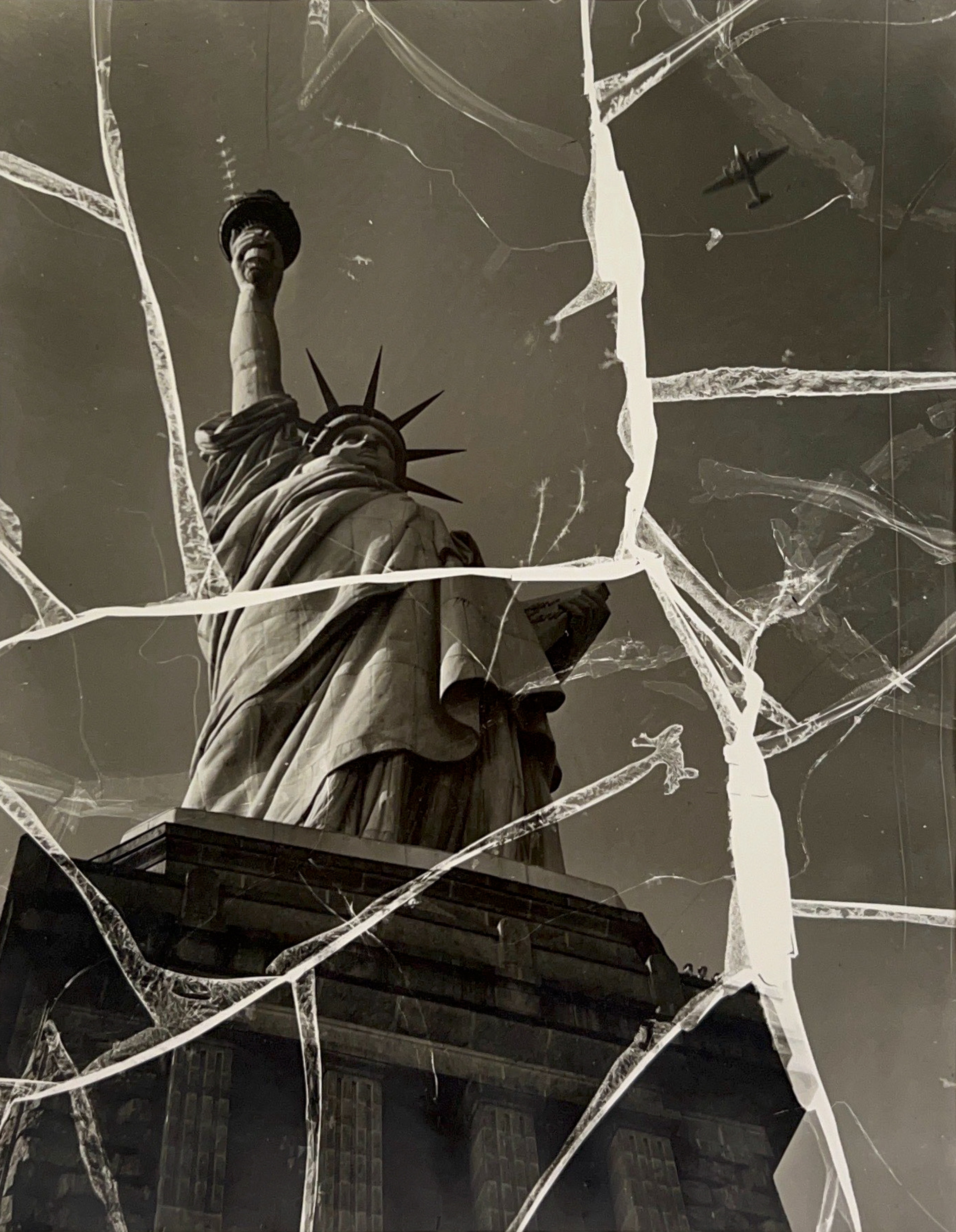 Black and white photograph of the Statue of Liberty from a low angle. The photograph has white streaks all over the surface, making it look cracked