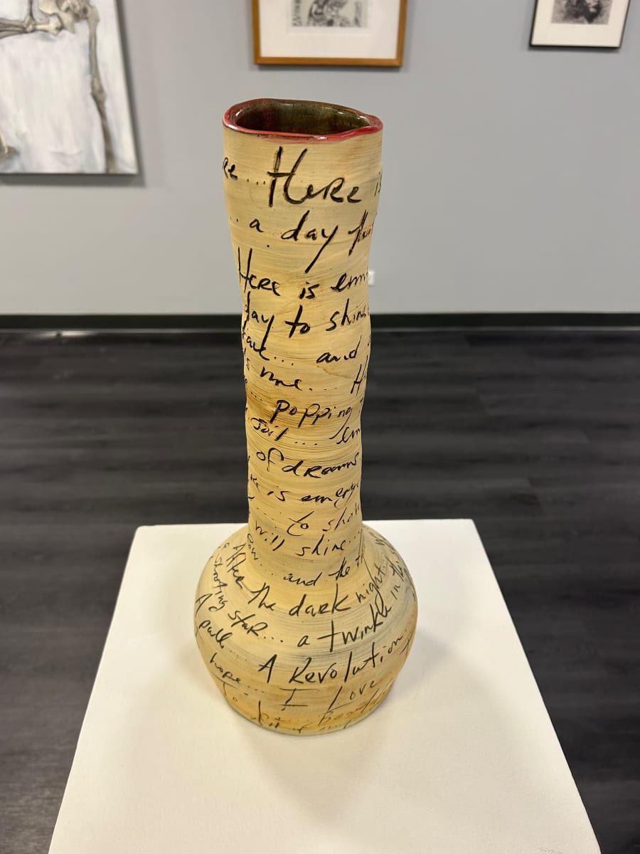 Ceramic vase with a bulbous base and tall neck. The vase is beige with black writing covering the entire outside and the inside has a maroon glaze.