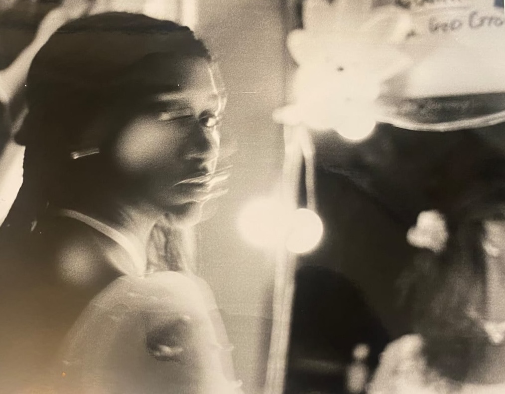 Black and white blurred photo of a woman looking over her shoulder with her reflection in a mirror in the background.