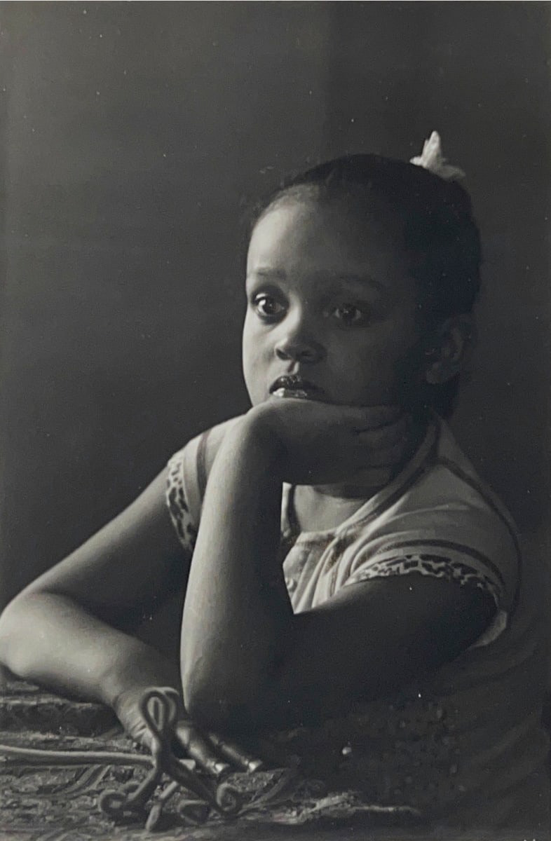 Black and white photograph of a young girl sitting with her chin in her hand