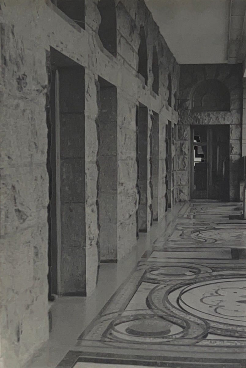 Black and white photograph of a building's hallway with stone walls and a patterned floor.