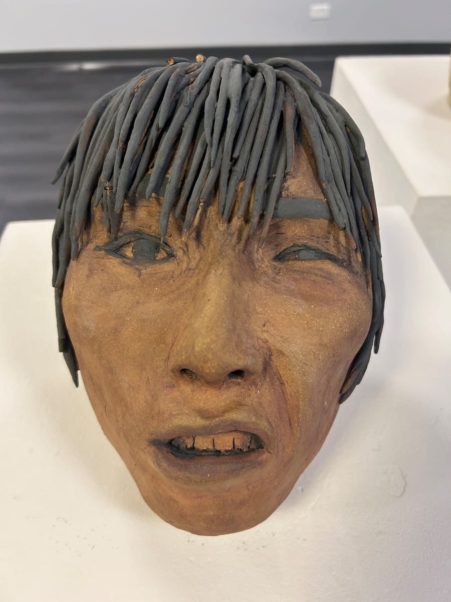 Ceramic head of a man who is man is making a distraught face, squinting one eye with his mouth open. The man has brown skin and black hair and eyes.