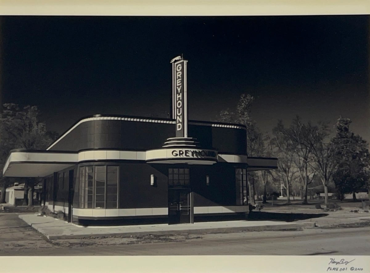 Black and white photograph of a Greyhound station with trees in the background and a dark sky