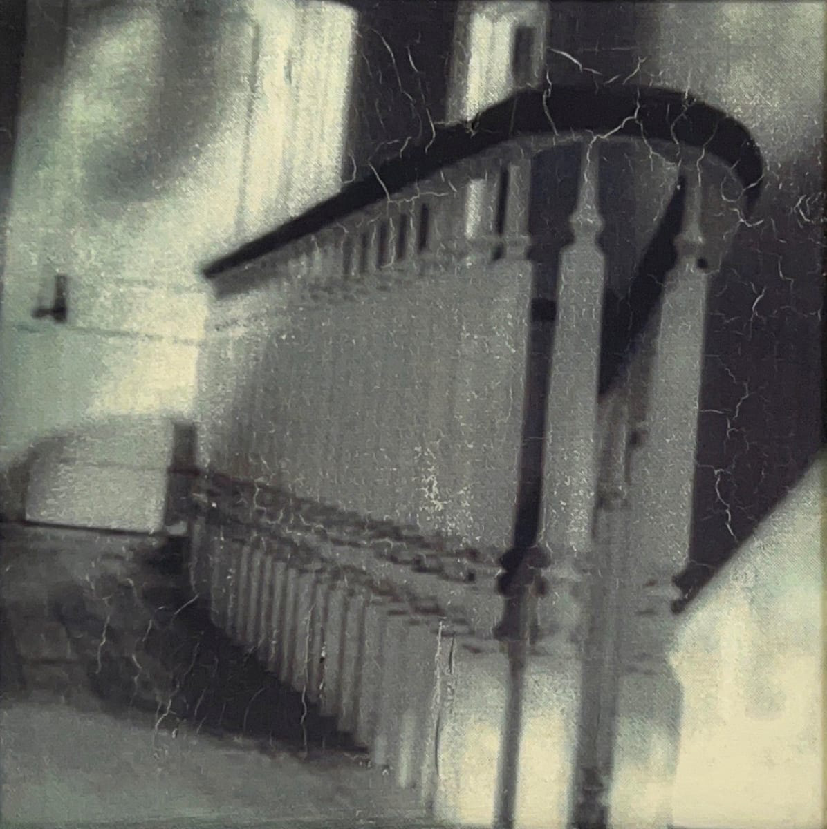 Black and white photographic print of a stairwell bannister and top floor landing. The surface of the image is cracked in many places.