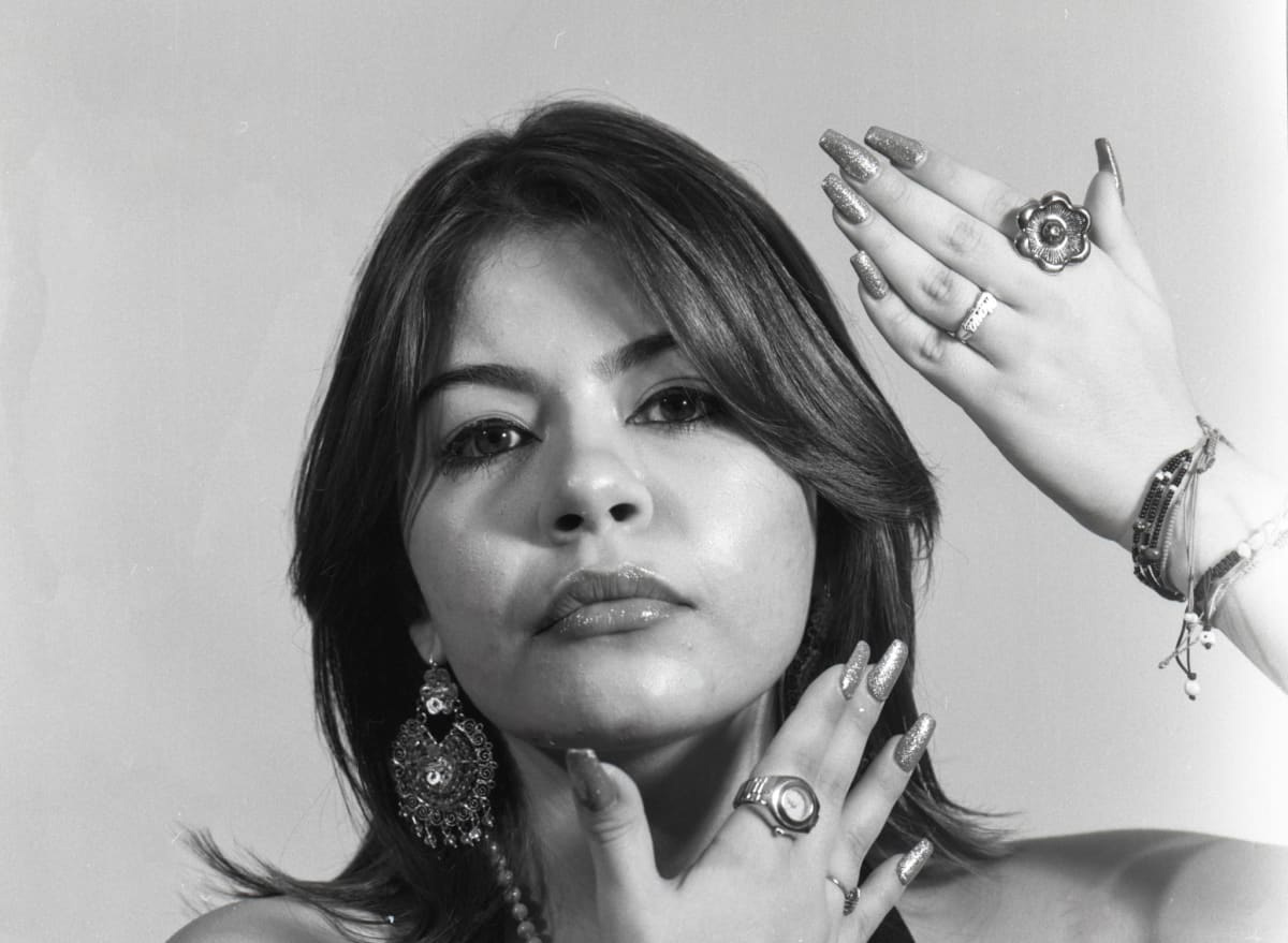 Black and white photograph of a woman with her hands surrounding her face, wearing lots of jewelry