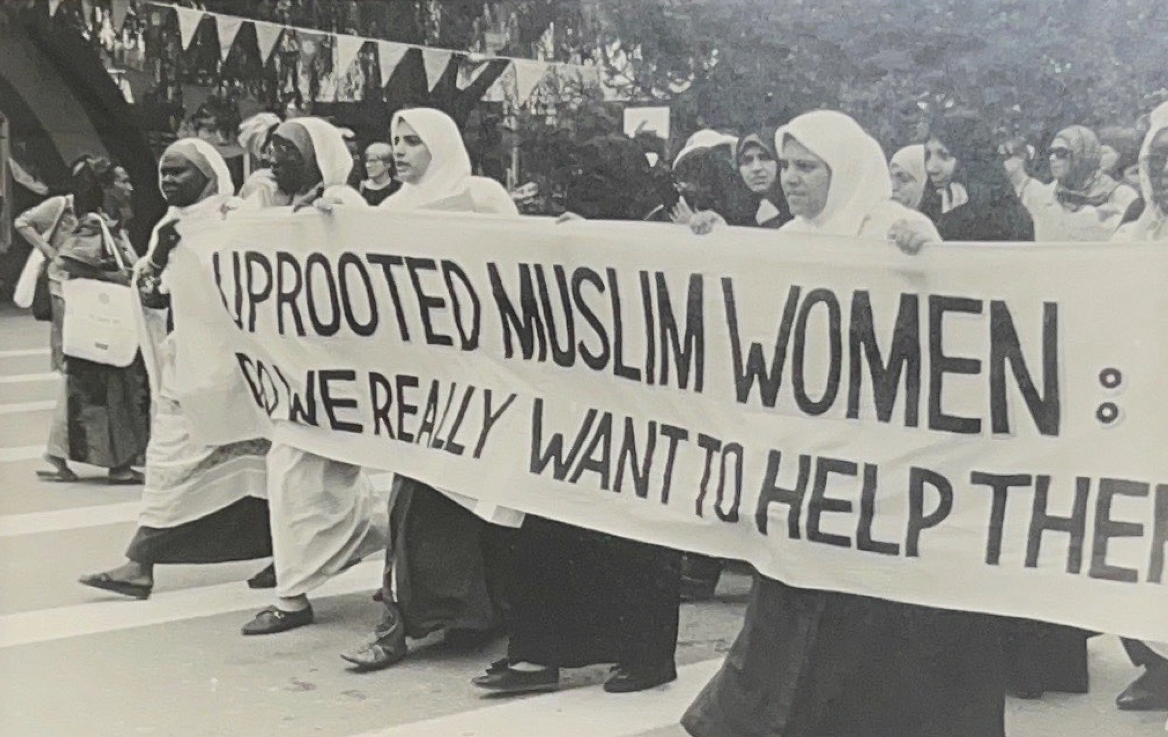 Black and white photo of a group of women marching and holding a large banner, partially cut off by the photo that reads "uprooted Muslim women: do we really want to help the" and the rest of the banner is cut off