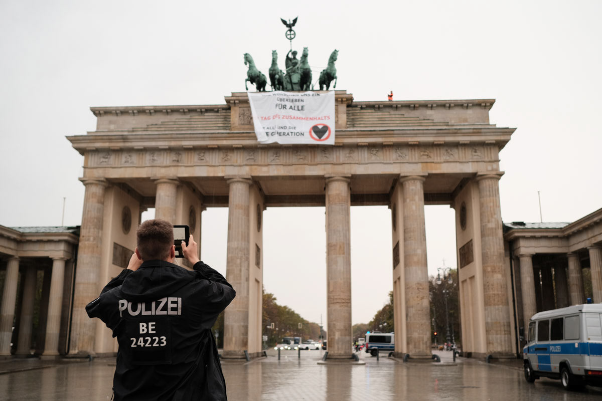 A police officer photographs two activists atop Brandenburg Gate