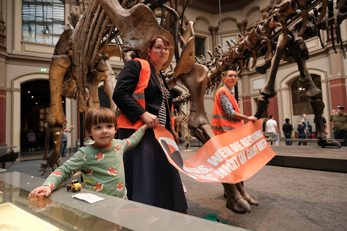 Two mothers, one holding her childs hand, glue themselves to a dinosaur exhibit at Berlin's Natural History Museum