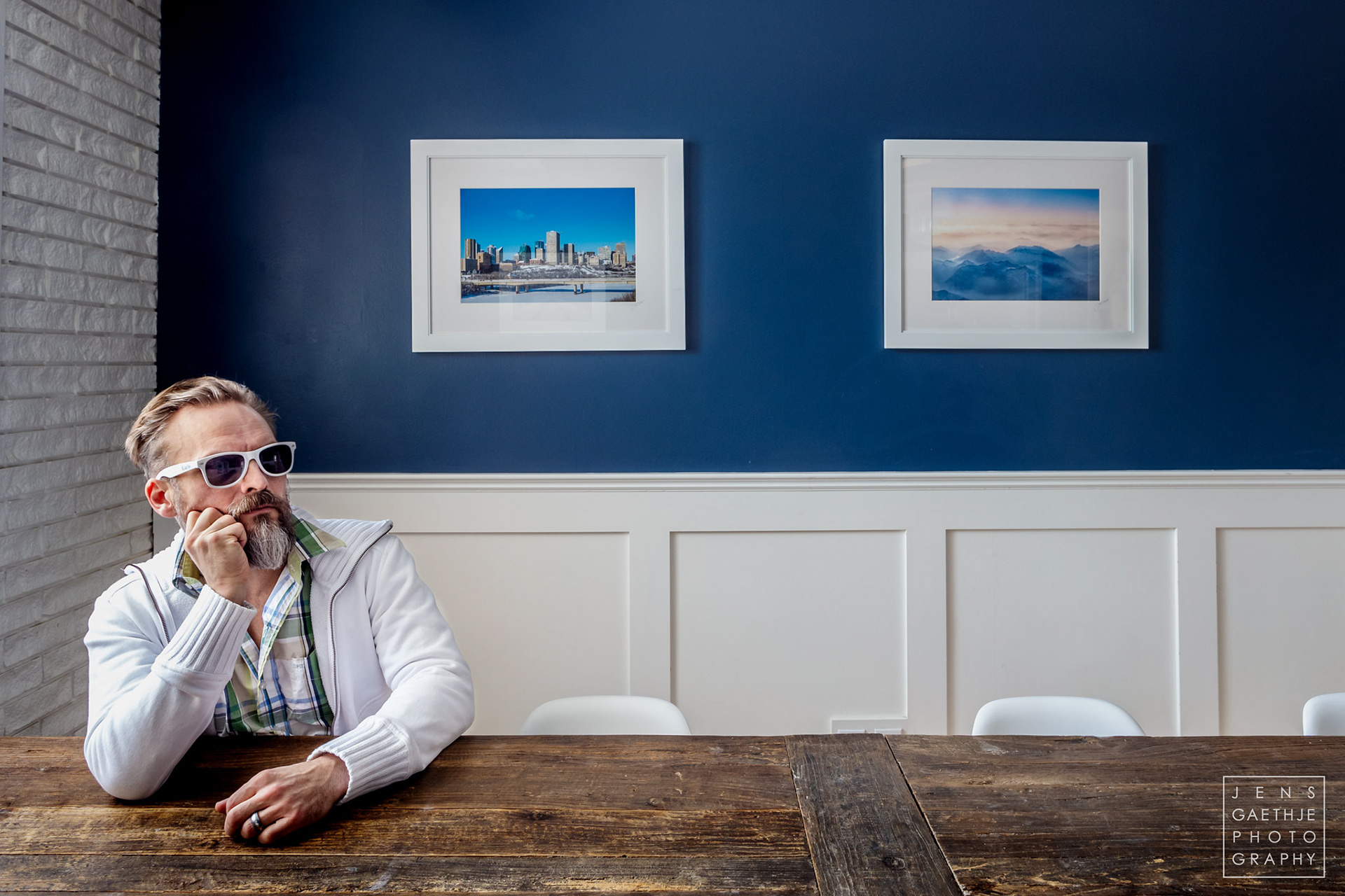 Fine Art Landscape Photographer Jens Gaethje sitting infront of 2 of his framed Artworks at the Little Brick Cafe in Edmonton, Alberta.