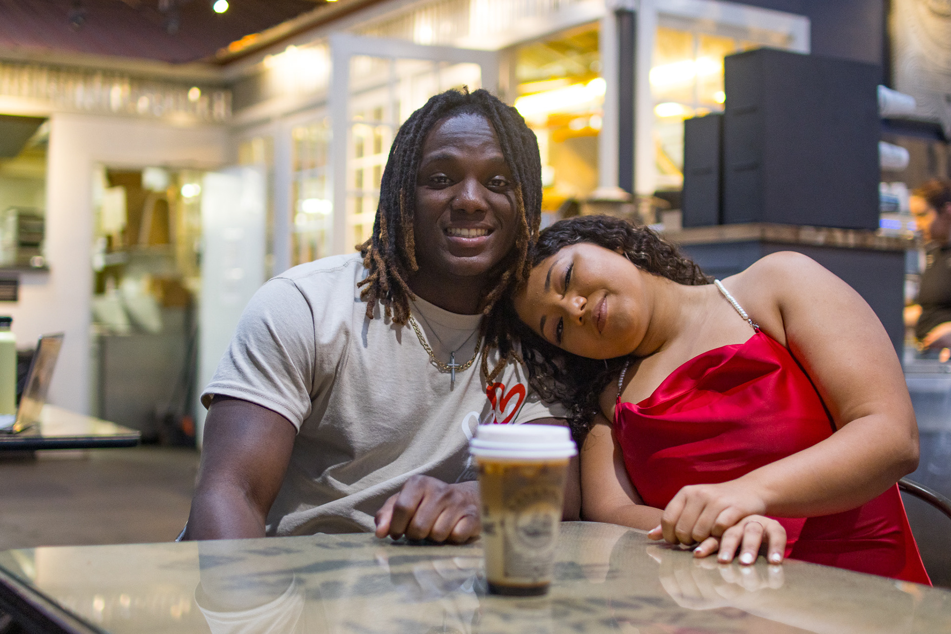 young couple sitting at table with girl's head on her partner's shoulder during rainy valentine's day photo shoot in coffee shop savannah georgia