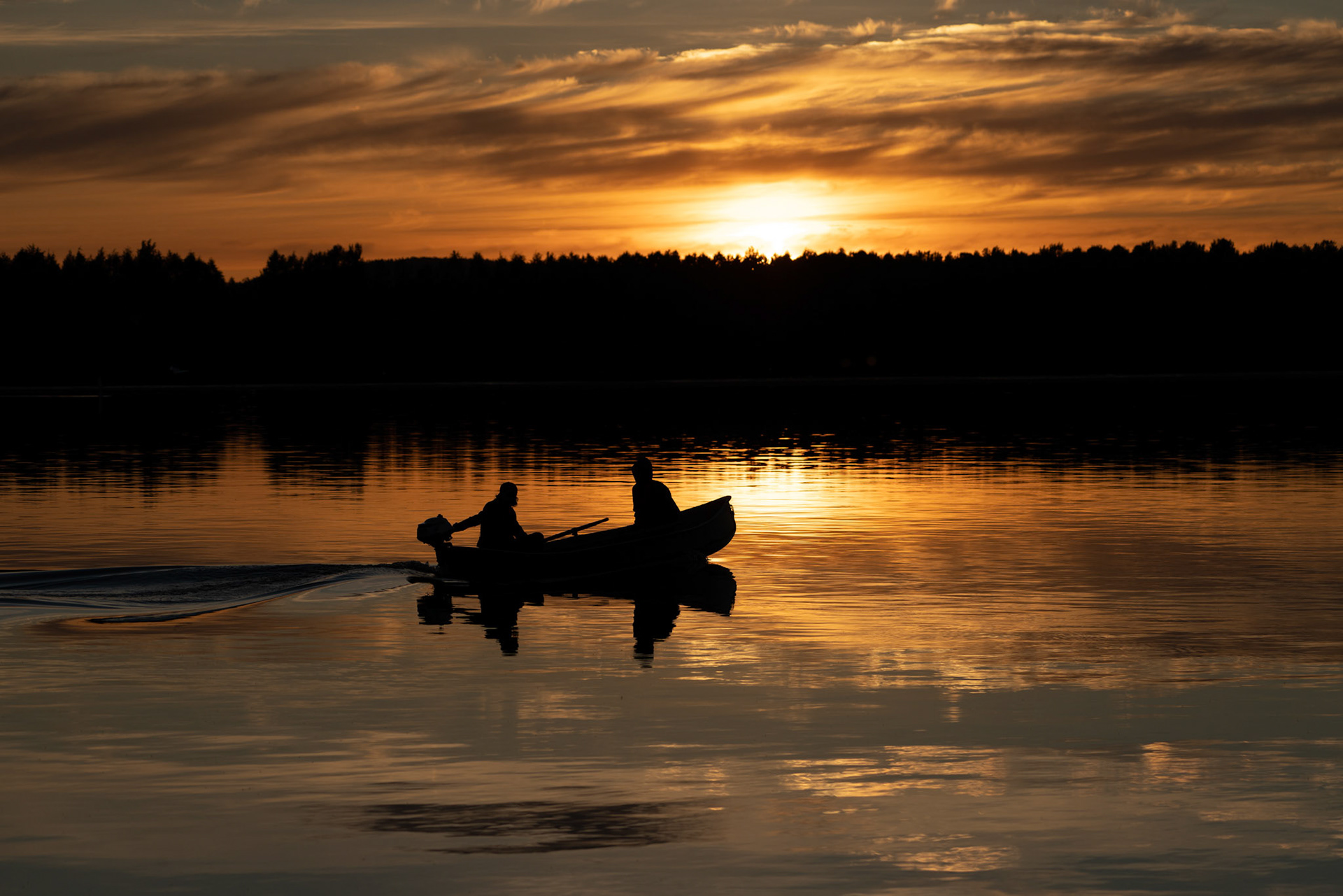 Couple of fishermen on a boat at sunset on a summer day in ... in backlight.