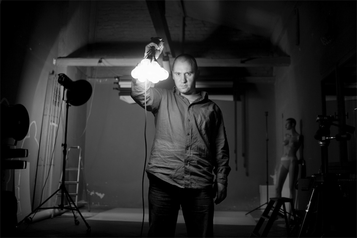 Radu Muntean holding a cluster of glowing light bulbs in a dark studio, photographed by Alex Gâlmeanu.
