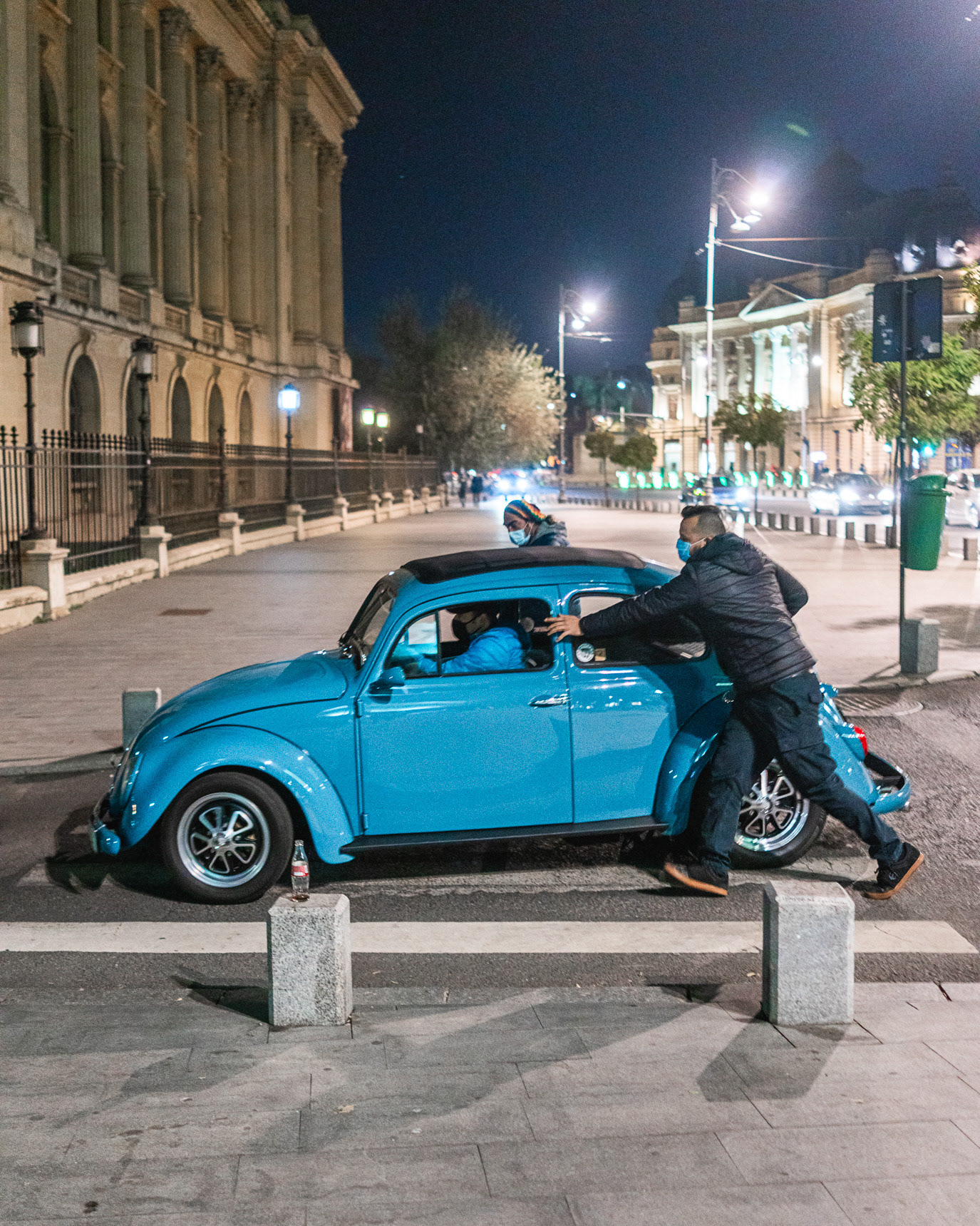 A man pushing a blue Volkswagen Beetle through an empty night street in Bucharest, Romania. Photograph by Alex Galmeanu.