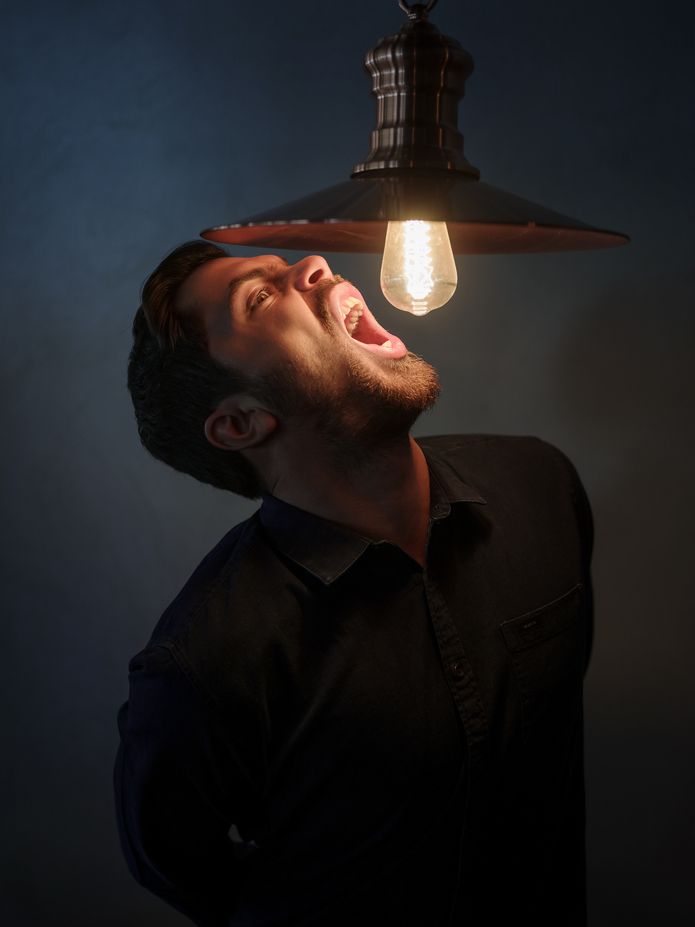 Alex Coteț opening his mouth beneath a bare light bulb, photographed by Alex Gâlmeanu.