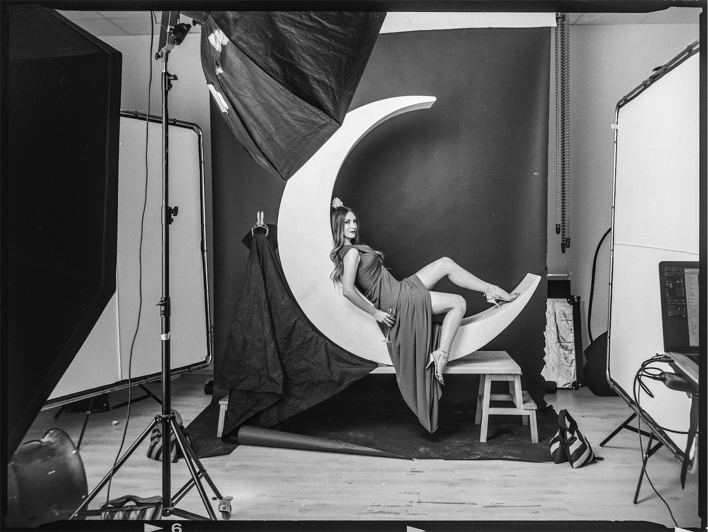 Adela Popescu reclining on a crescent-moon prop in a black-and-white studio scene, photographed by Alex Gâlmeanu.