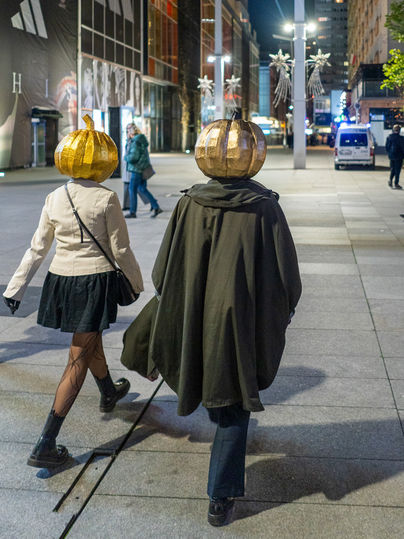 Two pedestrians wearing spherical gold headpieces on a Warsaw street in Poland. Photograph by Alex Galmeanu.