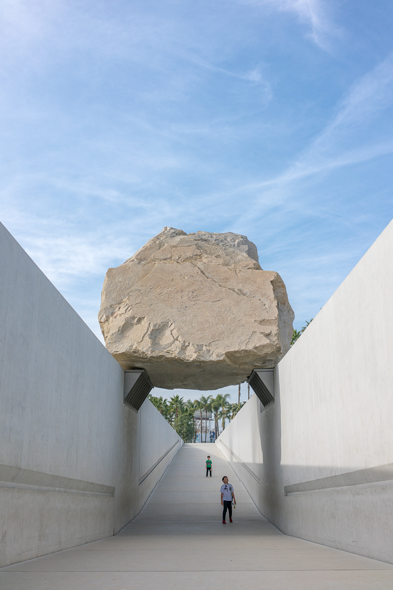A lone figure walking beneath a massive suspended boulder in Los Angeles, California. Photograph by Alex Galmeanu.