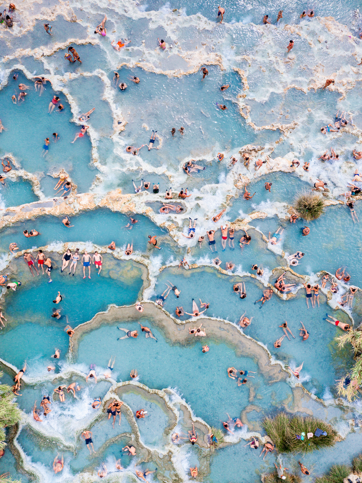 Bathers scattered across natural thermal pools seen from above in Saturnia, Italy. Photograph by Alex Galmeanu.