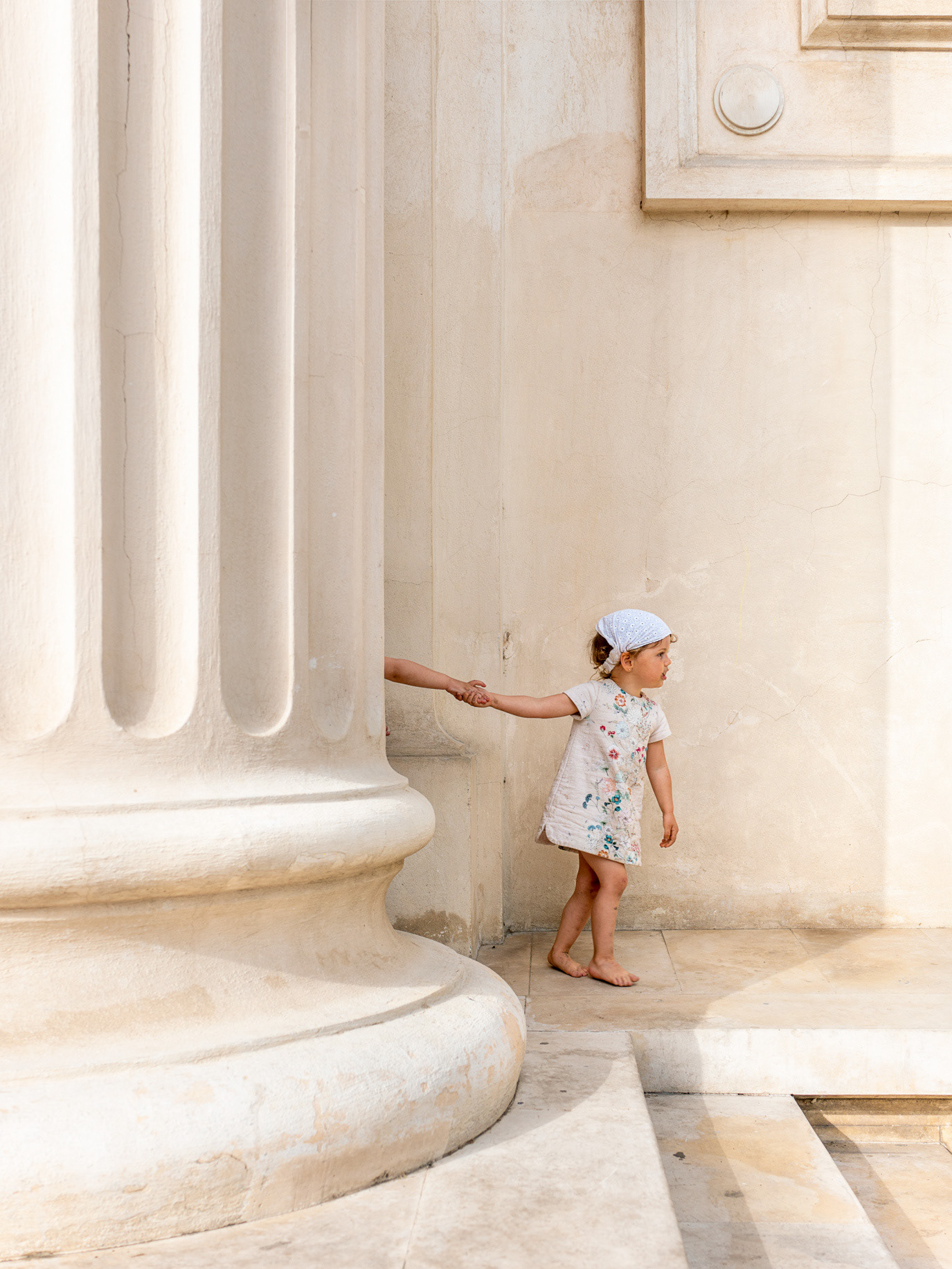 A small child standing beside monumental white columns in Bucharest, Romania. Photograph by Alex Galmeanu.